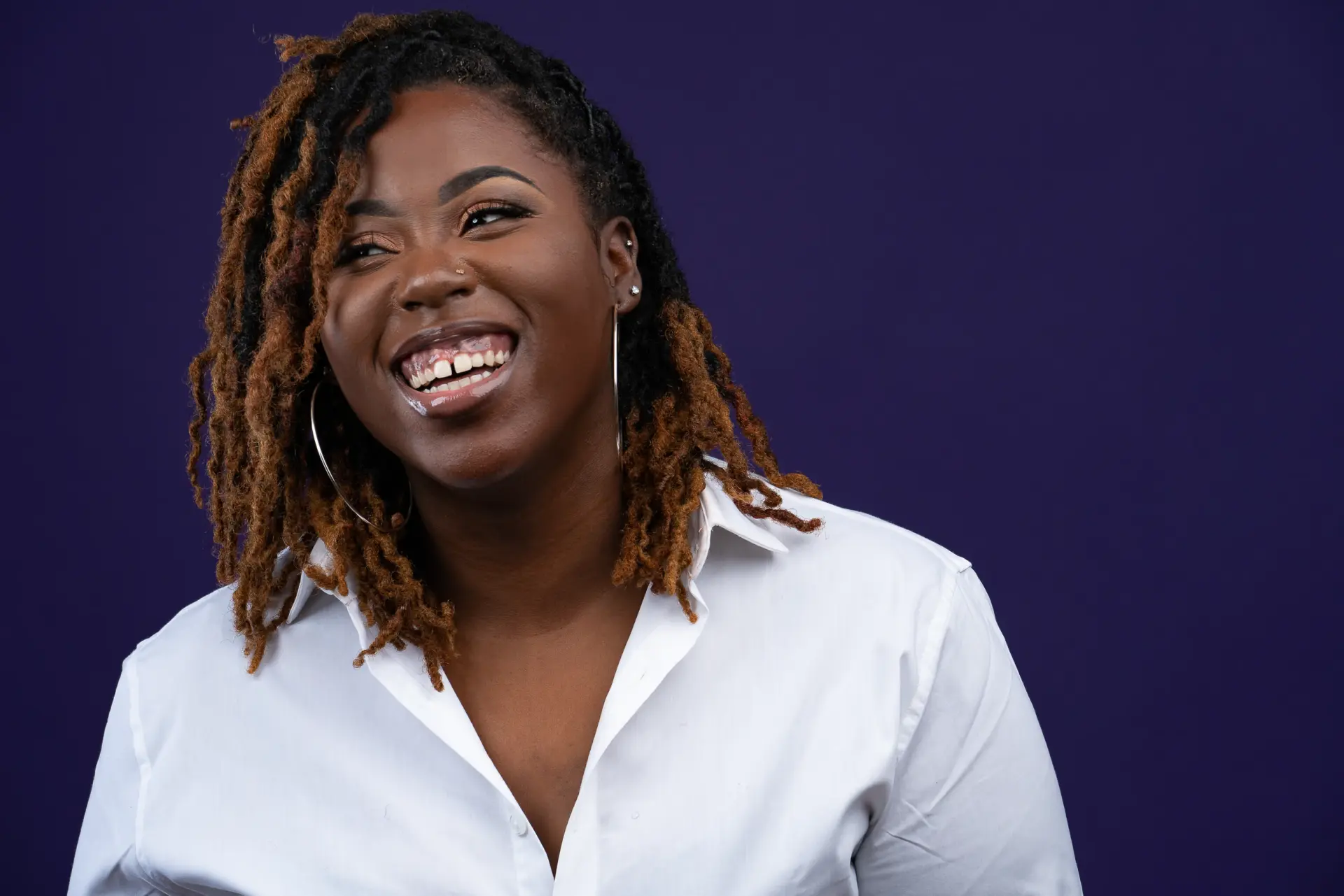Smiling woman with locs in a white shirt on a purple backdrop