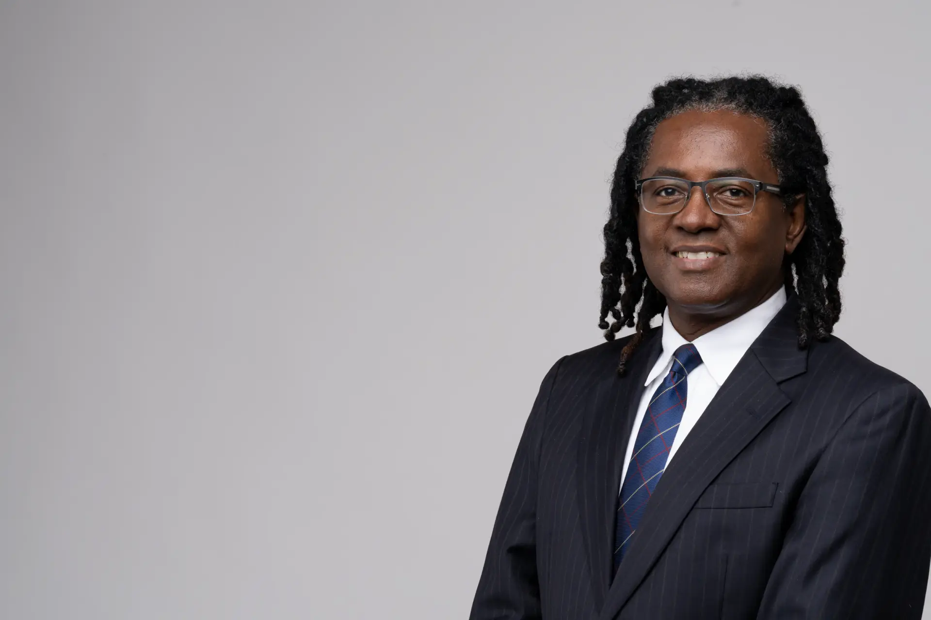 Confident business headshot of a man with locs and glasses in a navy suit