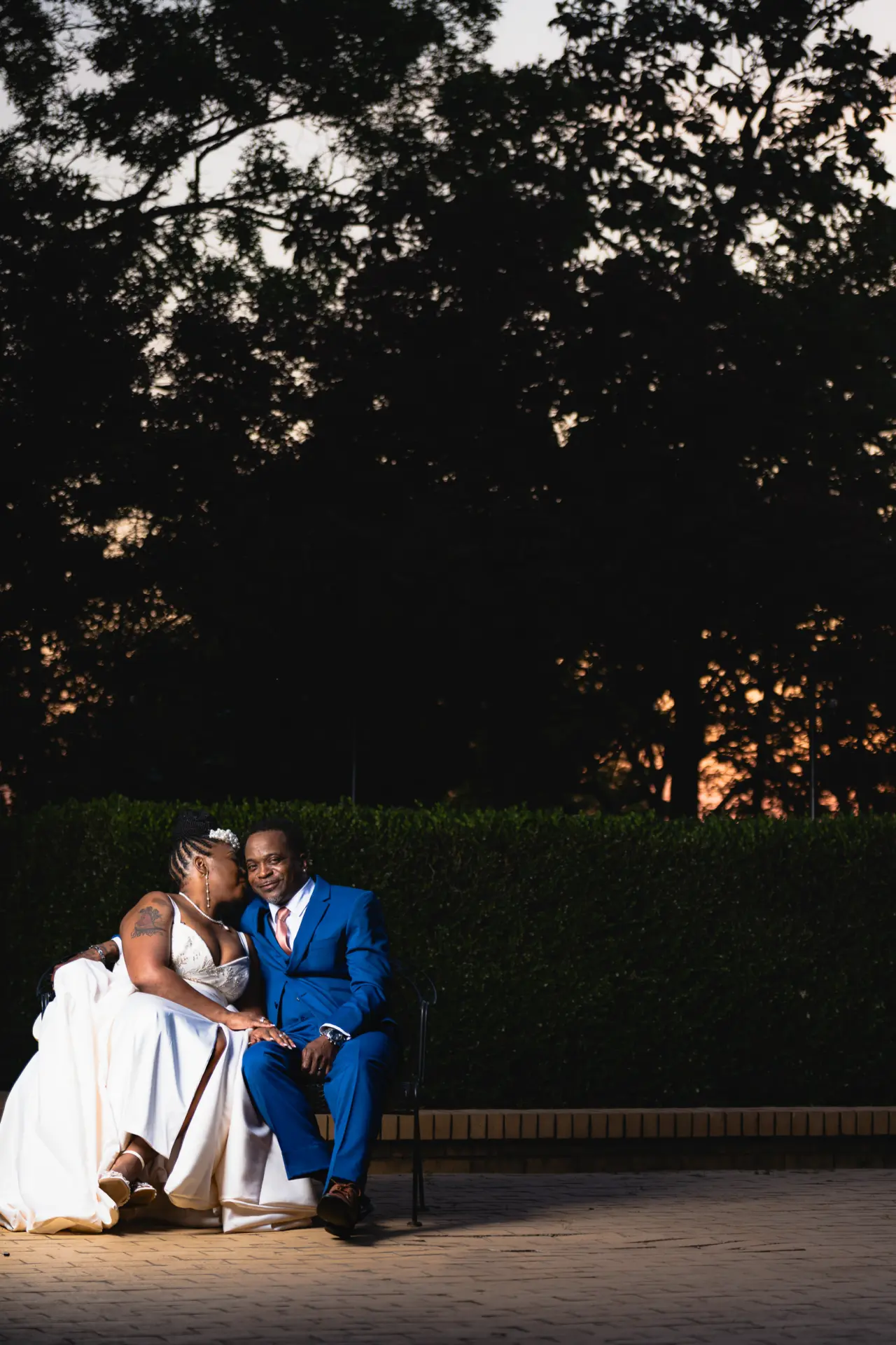 Newlyweds seated together on garden steps at dusk beneath tall trees