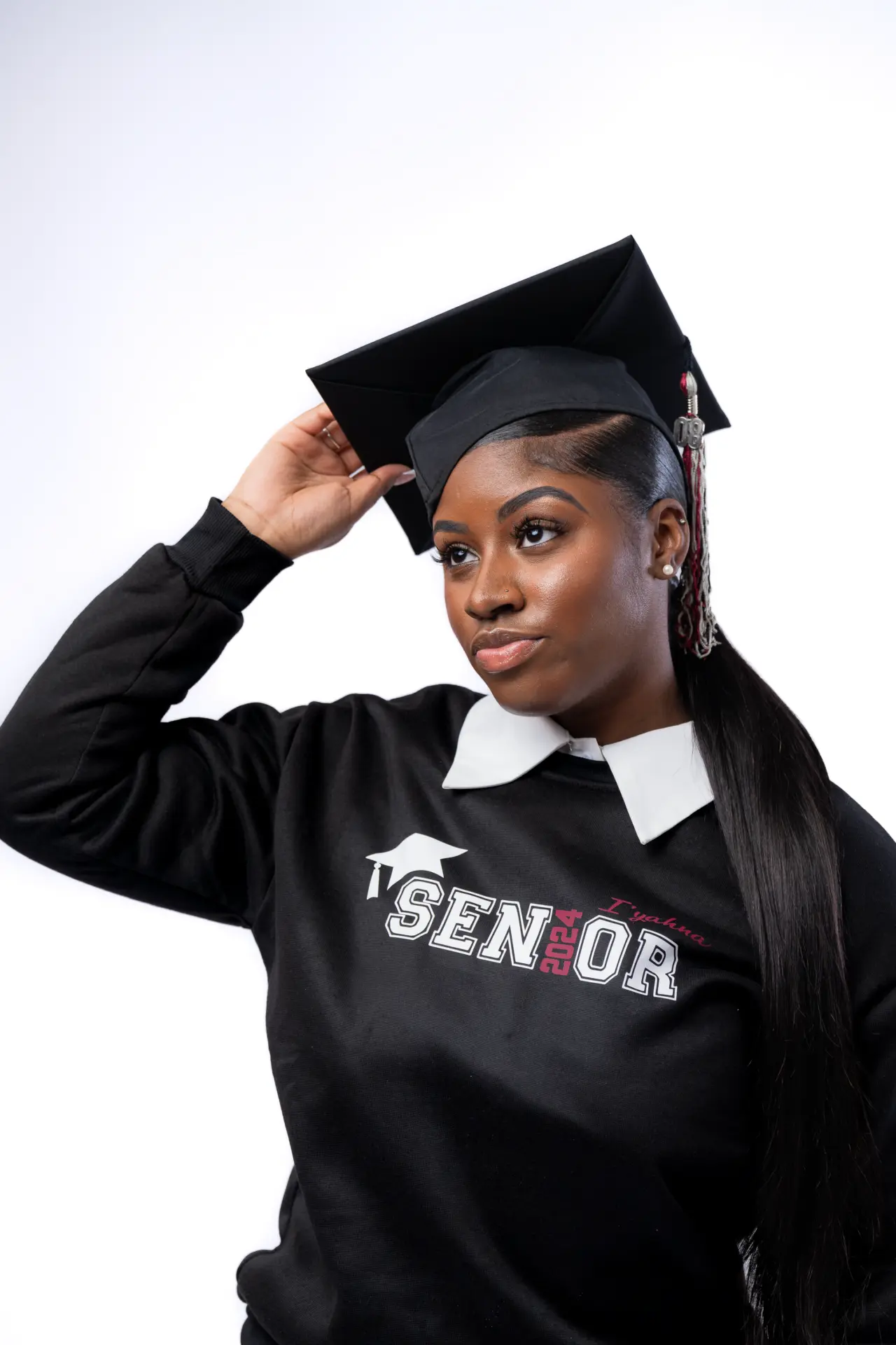 Graduate in a "Senior" sweatshirt adjusting her cap on white