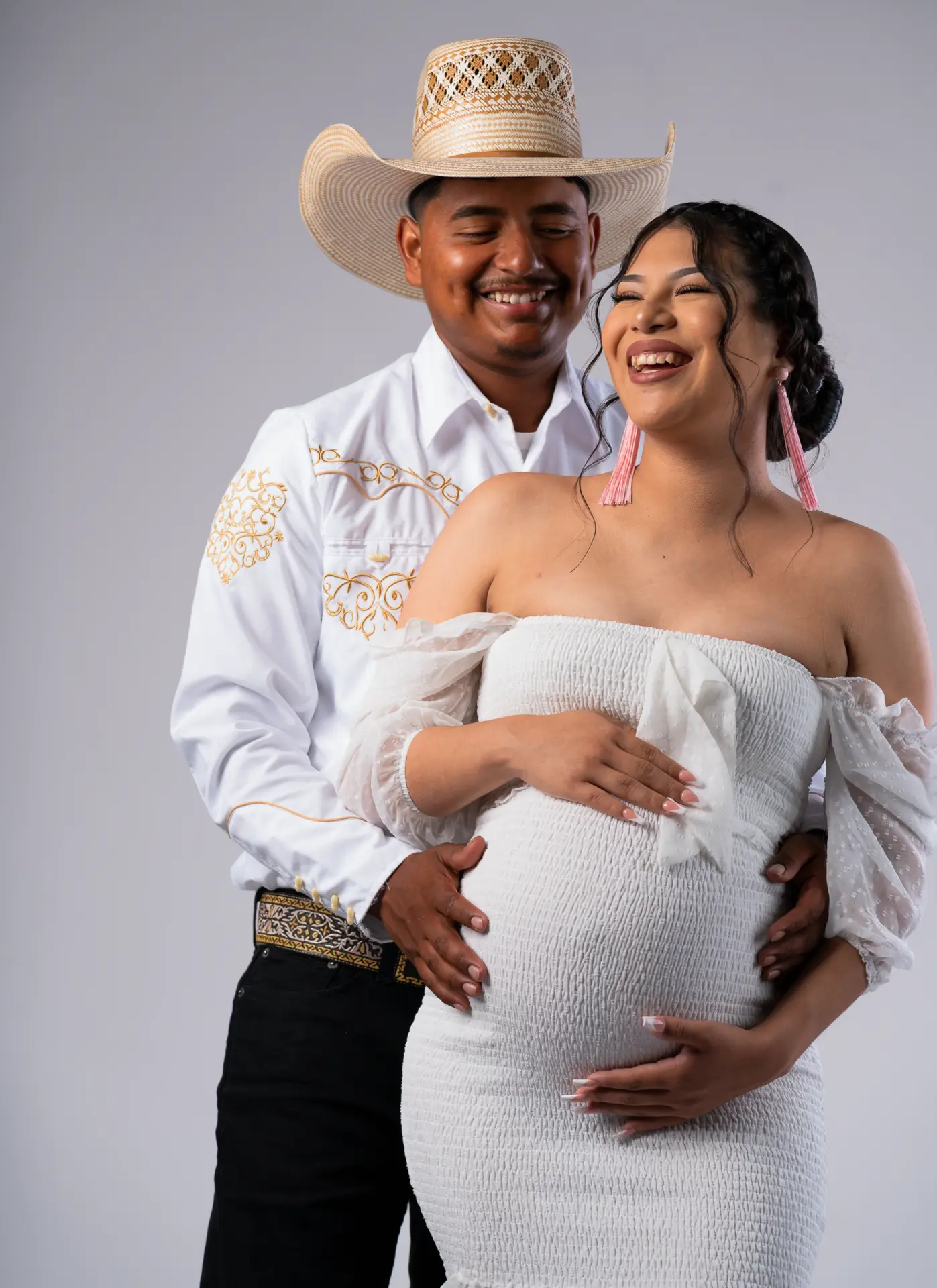 Expecting couple in western hats, mother in white lace holding her bump