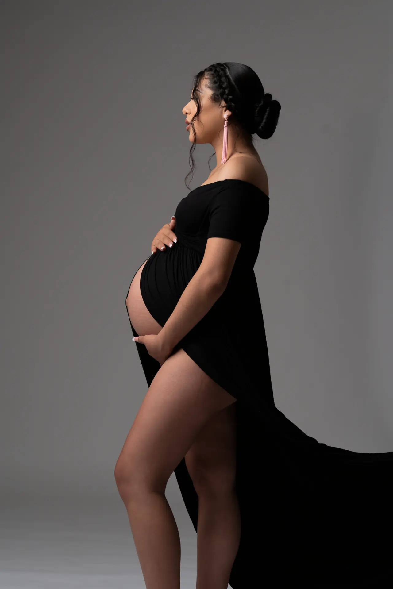 Pregnant woman in a flowing black gown posing in profile against a gray backdrop