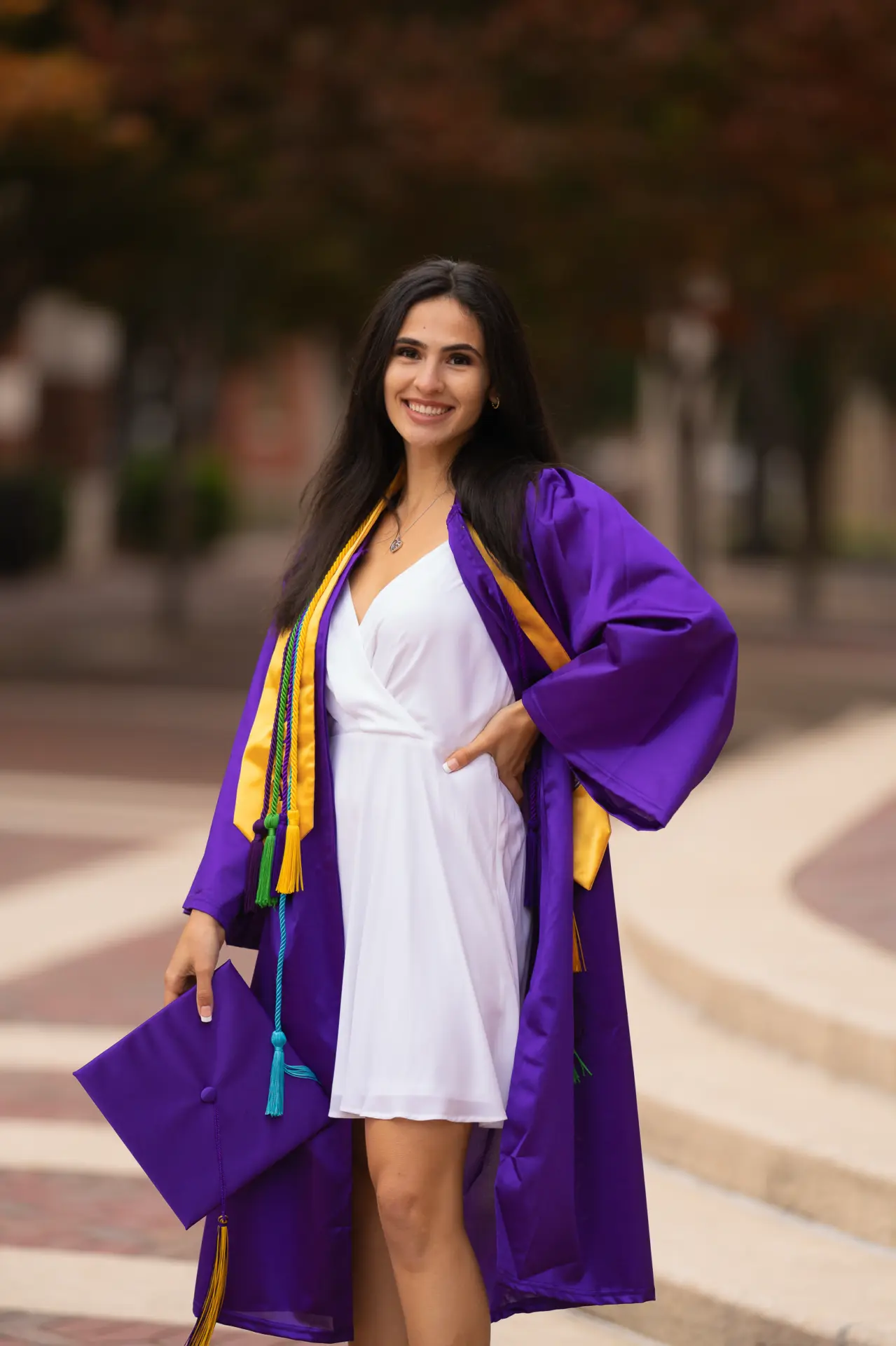 Graduate in a purple gown and gold stole by blooming trees