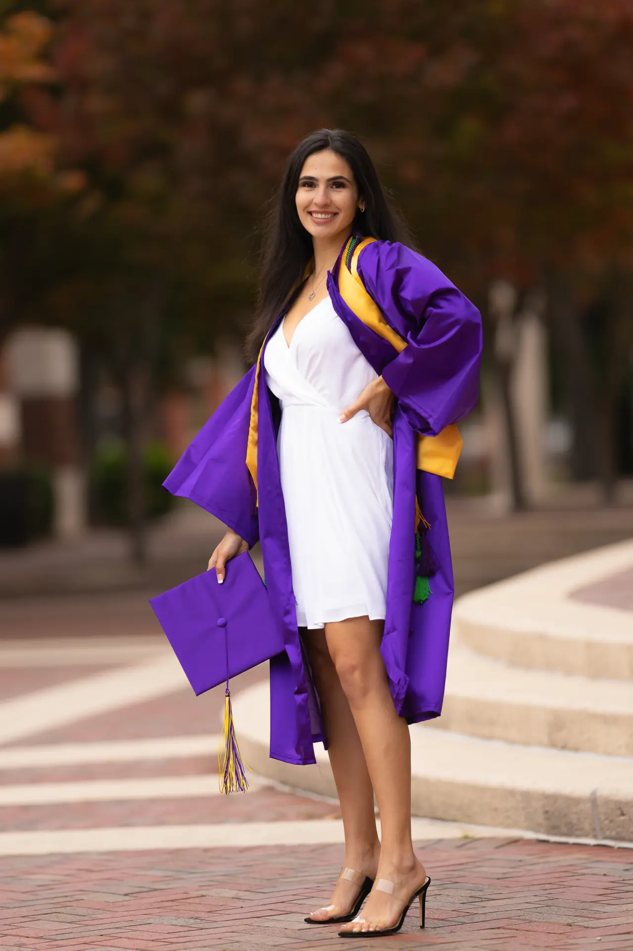 Graduate in a purple gown and white dress on brick campus steps