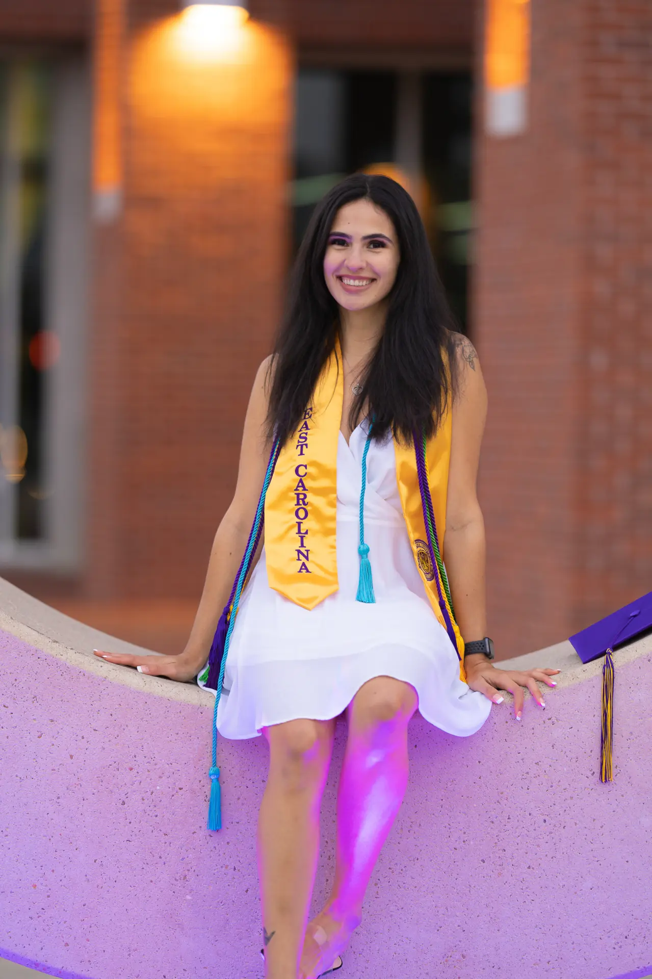 Graduate in a white dress and gold stole walking down campus steps