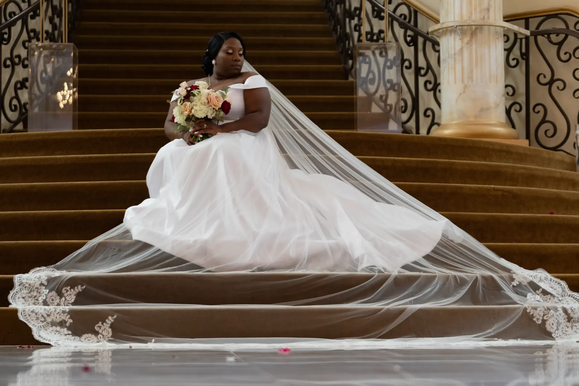 Bride in a long cathedral veil sits on a grand staircase