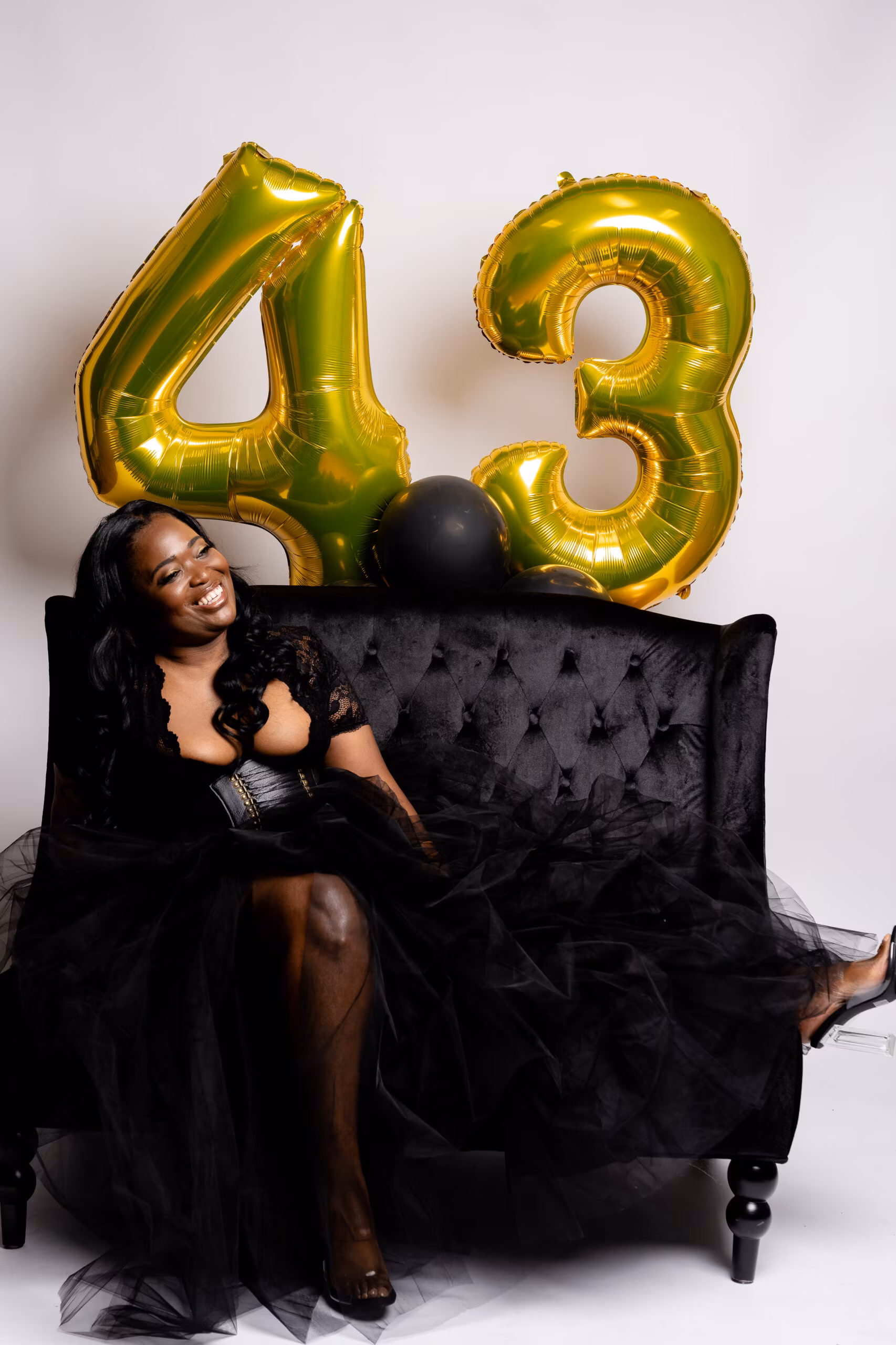 Woman on a black velvet couch with gold "43" balloons
