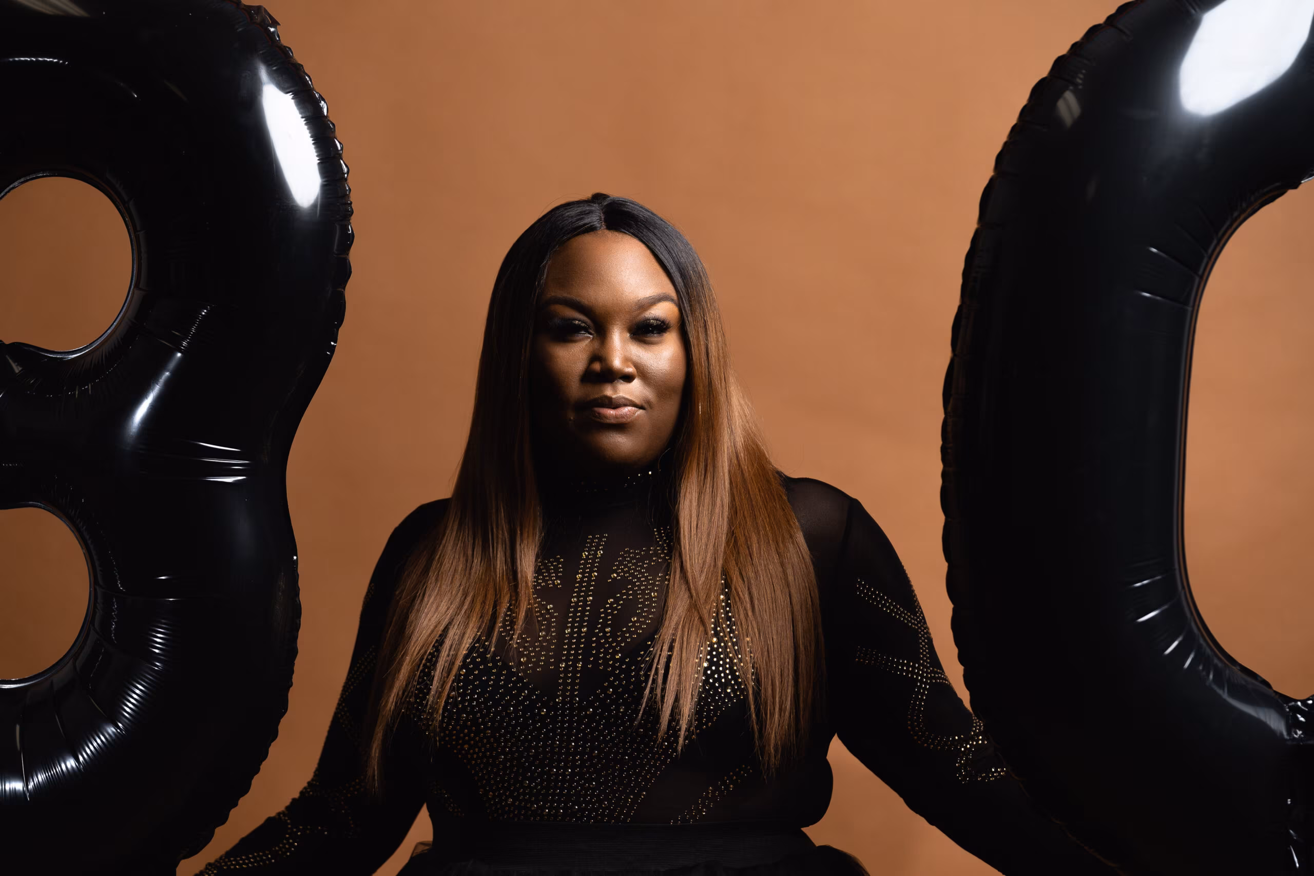 Woman between giant black "30" balloons against tan