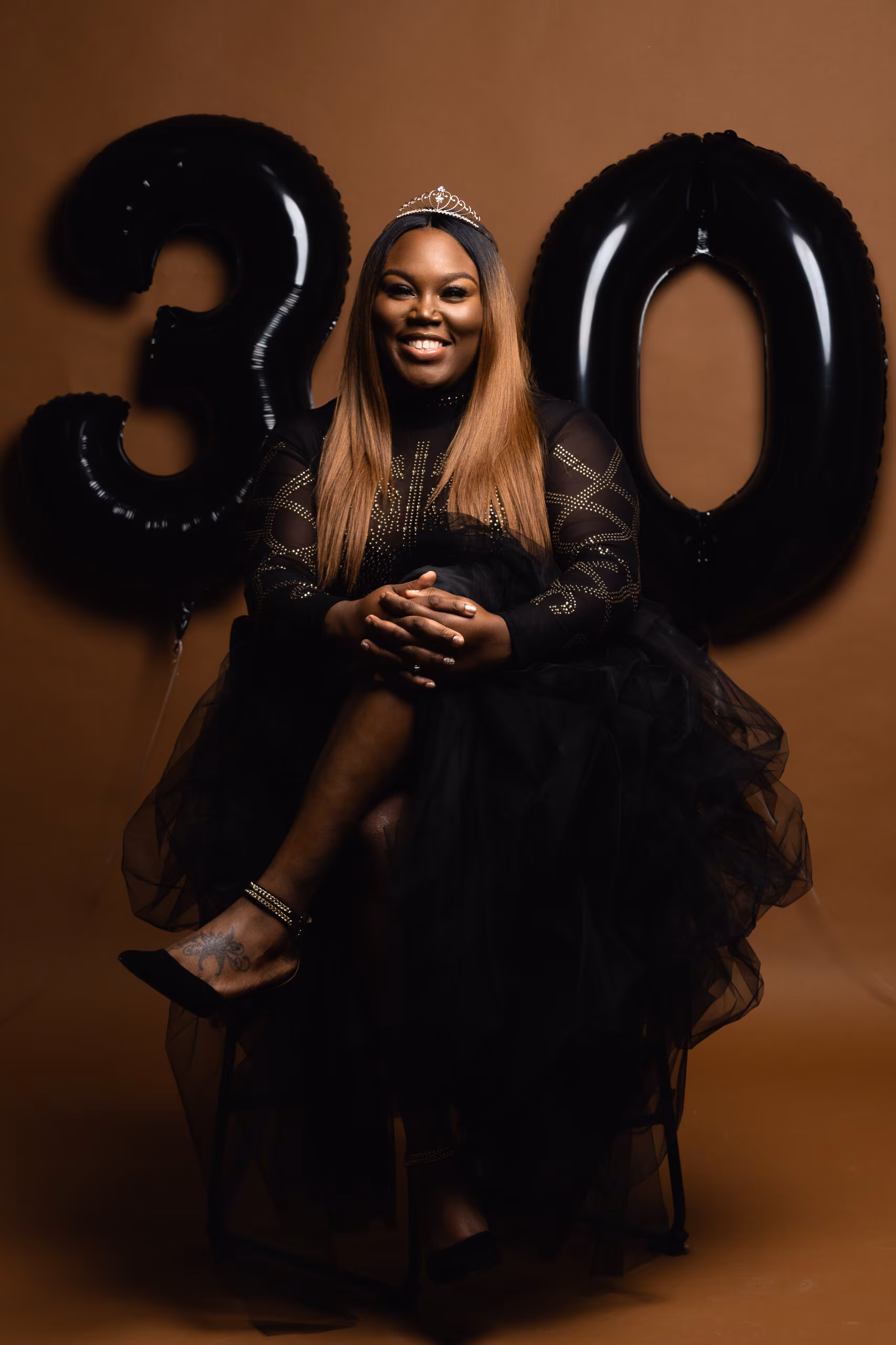 Woman in a black gown seated between black "30" balloons