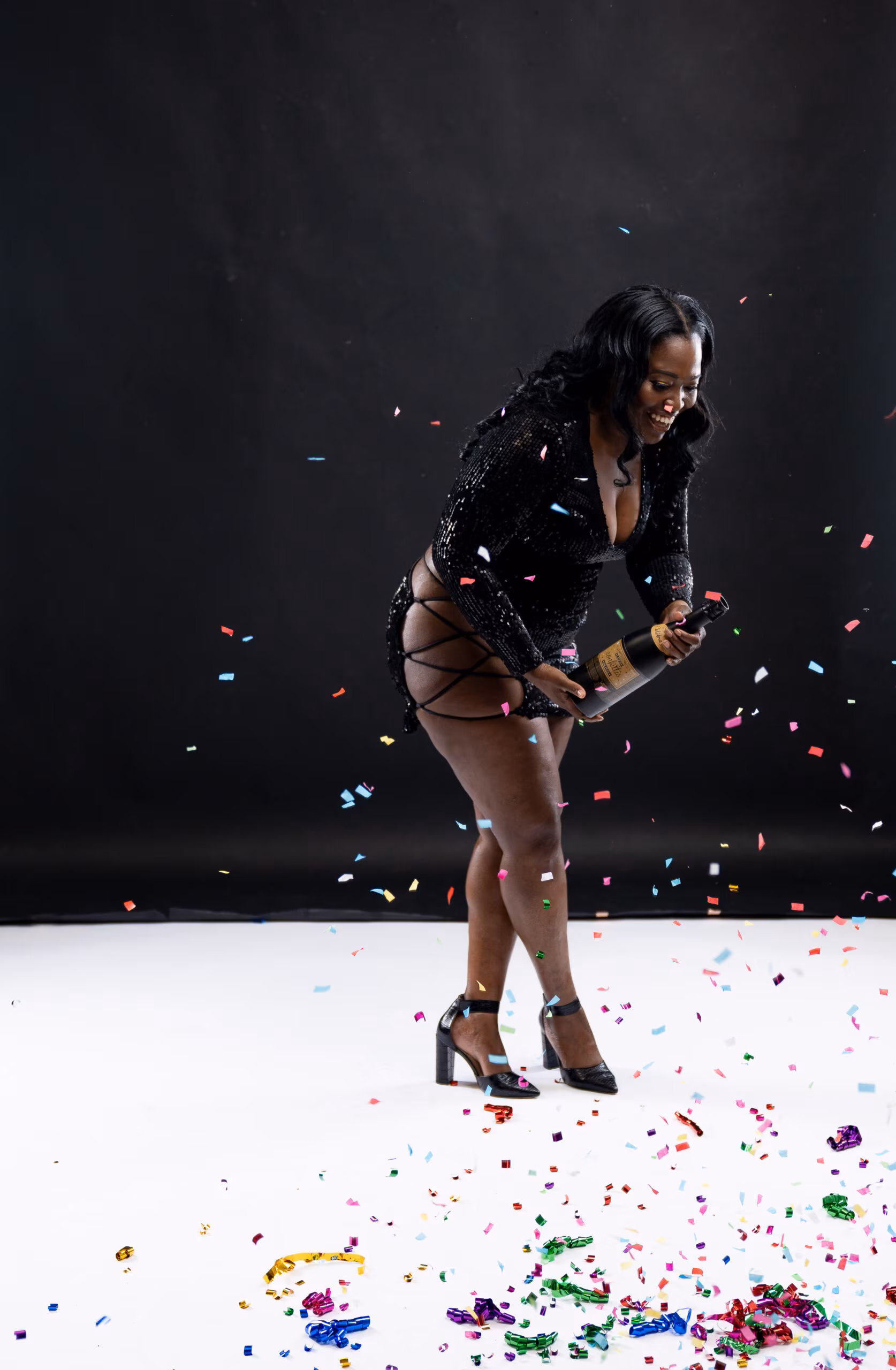 Woman in black kicking up confetti on a dark birthday set