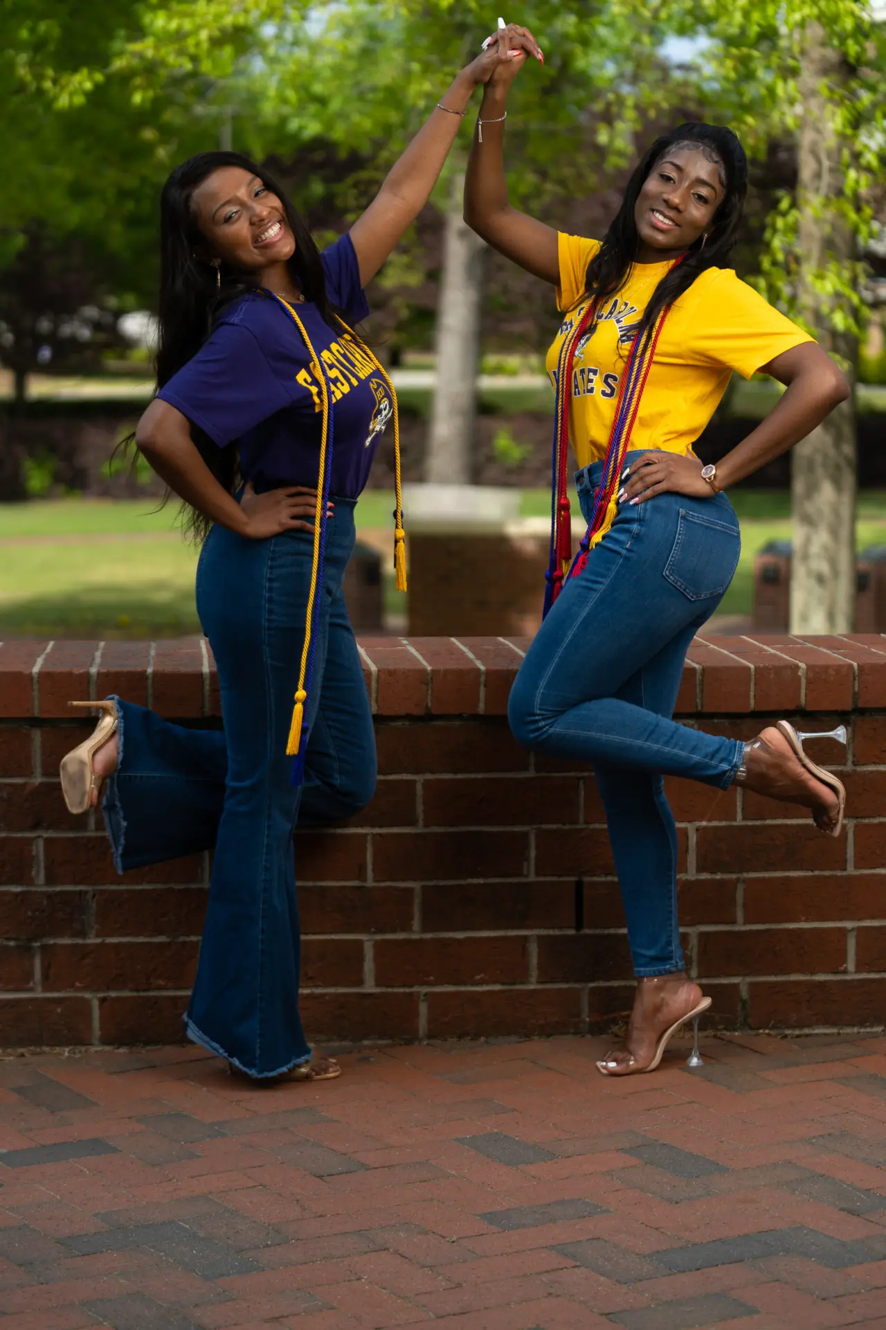 Two friends in graduation stoles jumping in celebration on campus