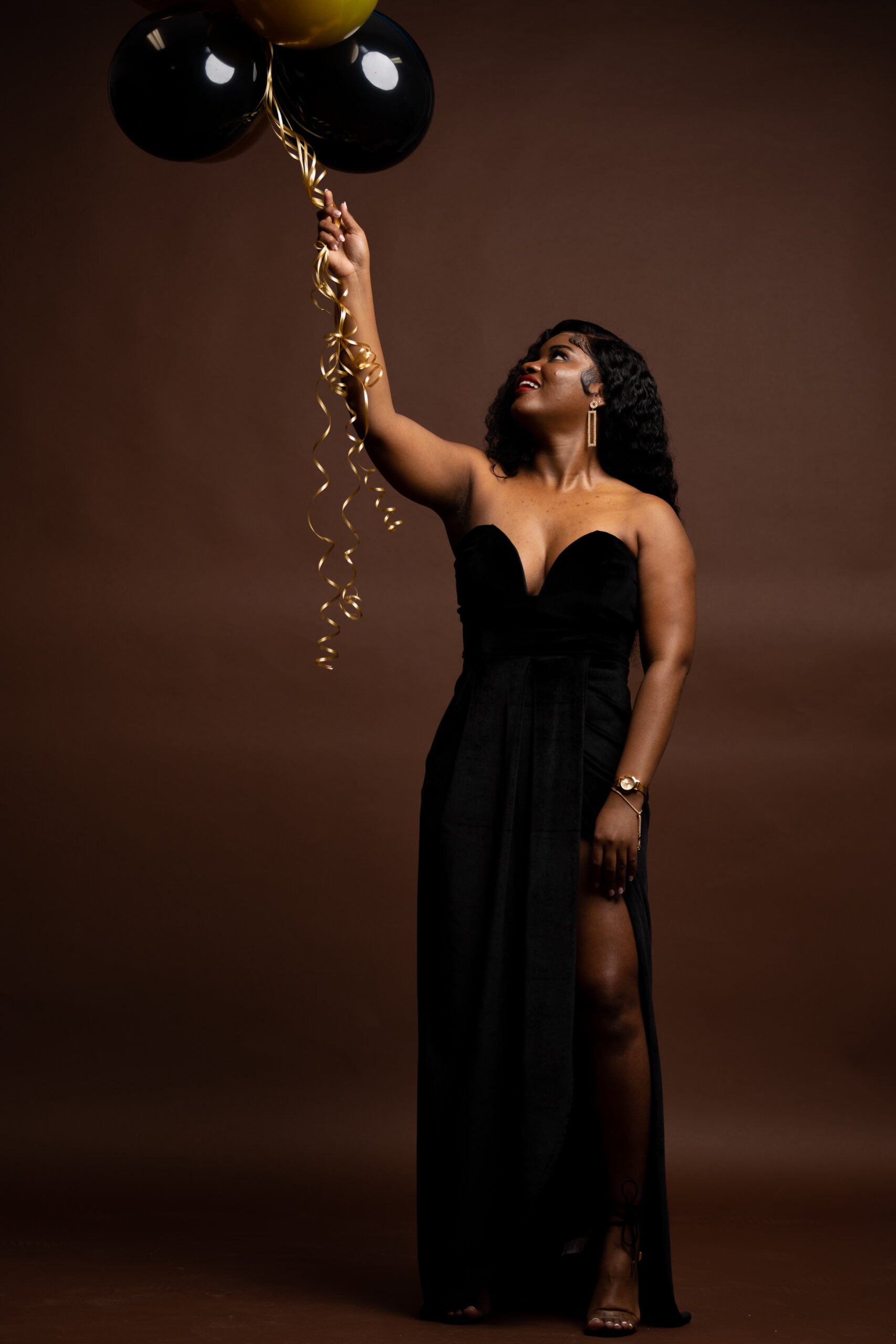 Woman in a black gown holding black balloons against brown
