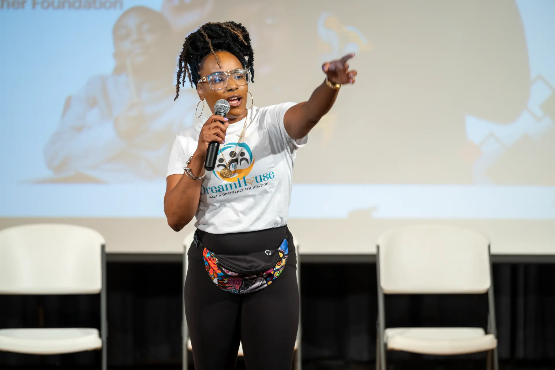 Speaker with a microphone addressing an audience before a projection screen