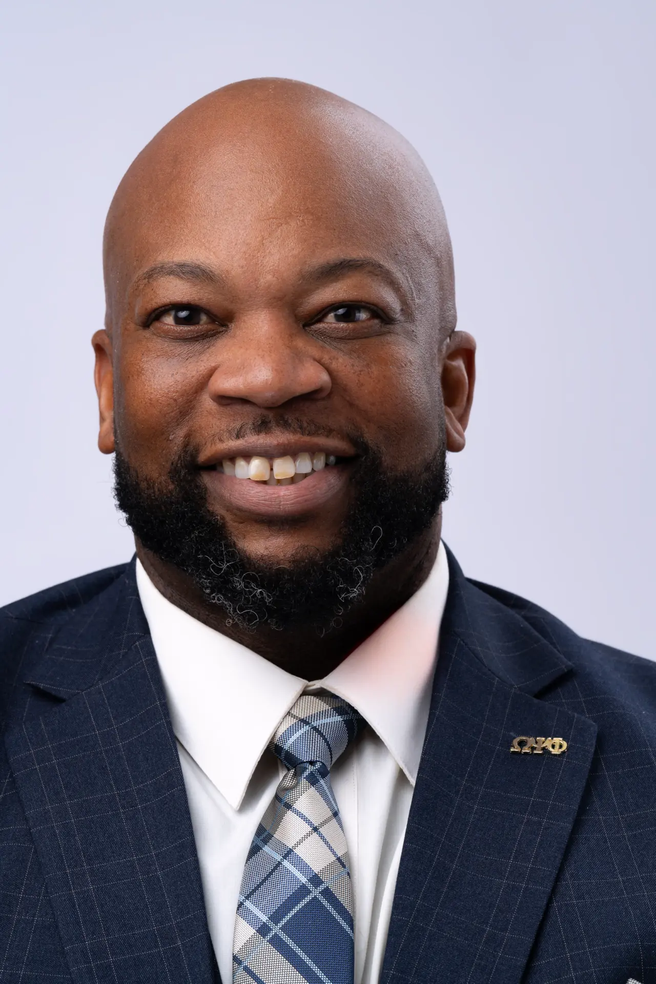 Smiling bald man in a navy suit and striped tie, studio headshot
