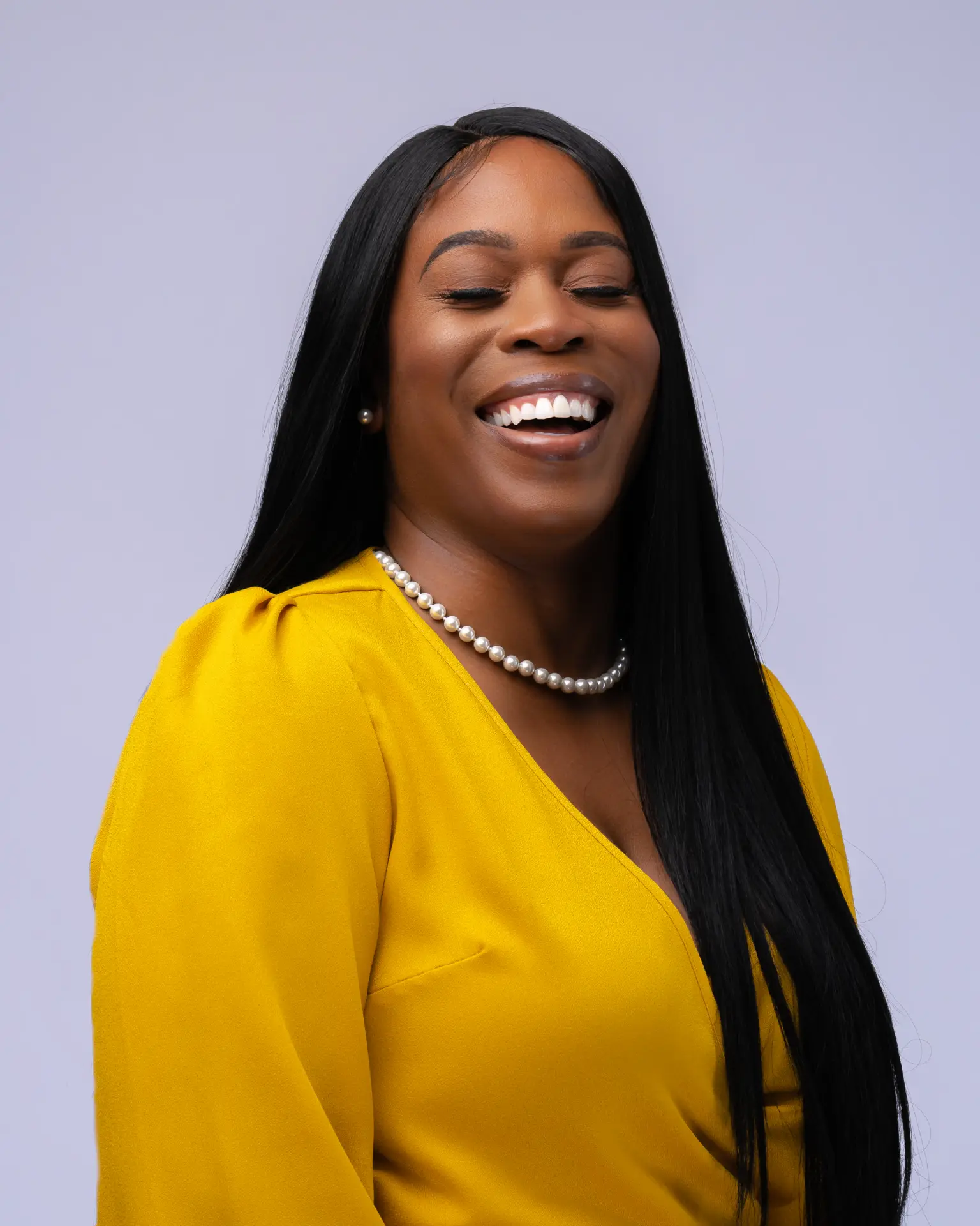 Woman in a yellow blouse smiling on a soft lavender backdrop