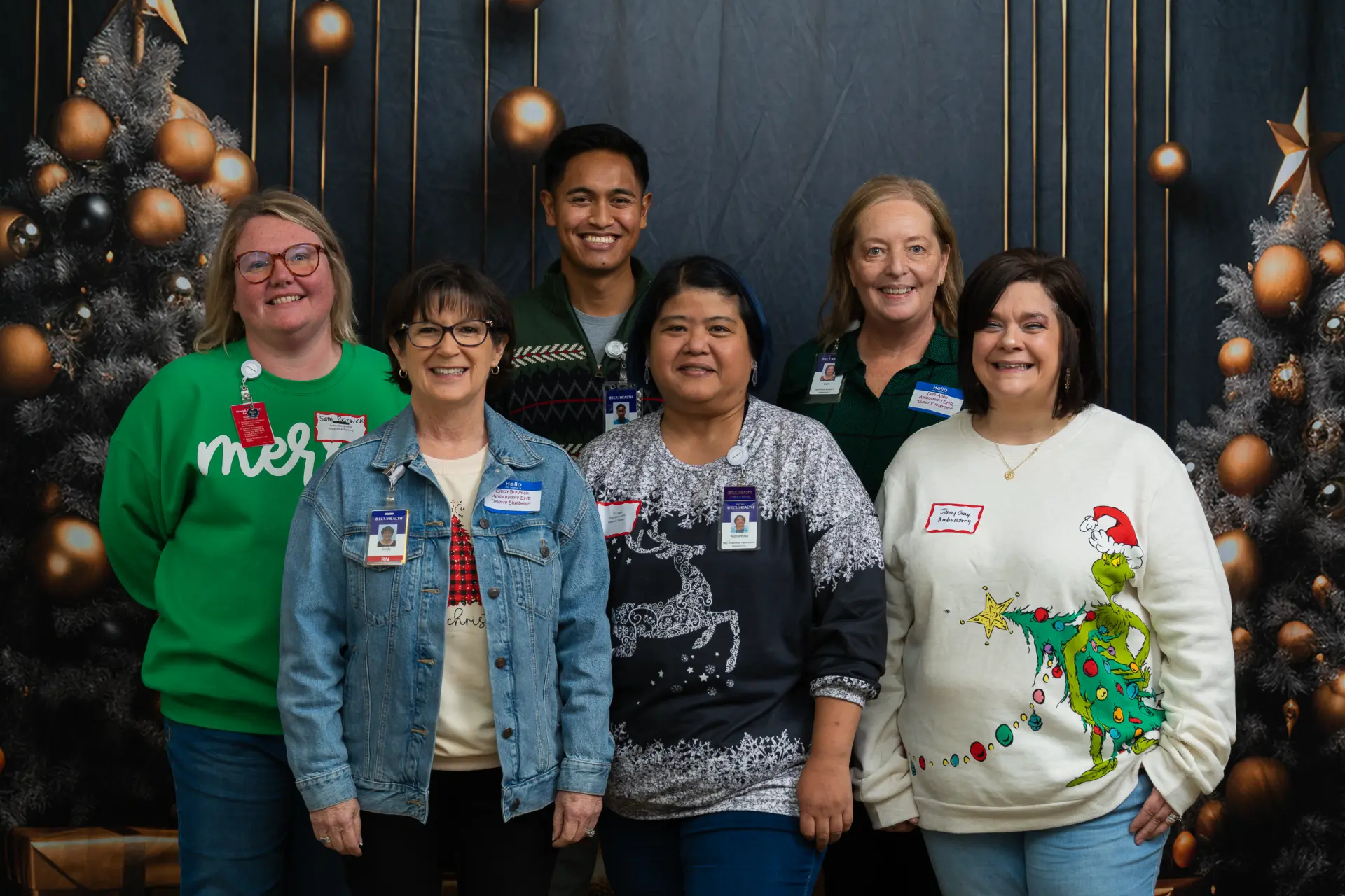 Group in holiday sweaters smiling under string lights