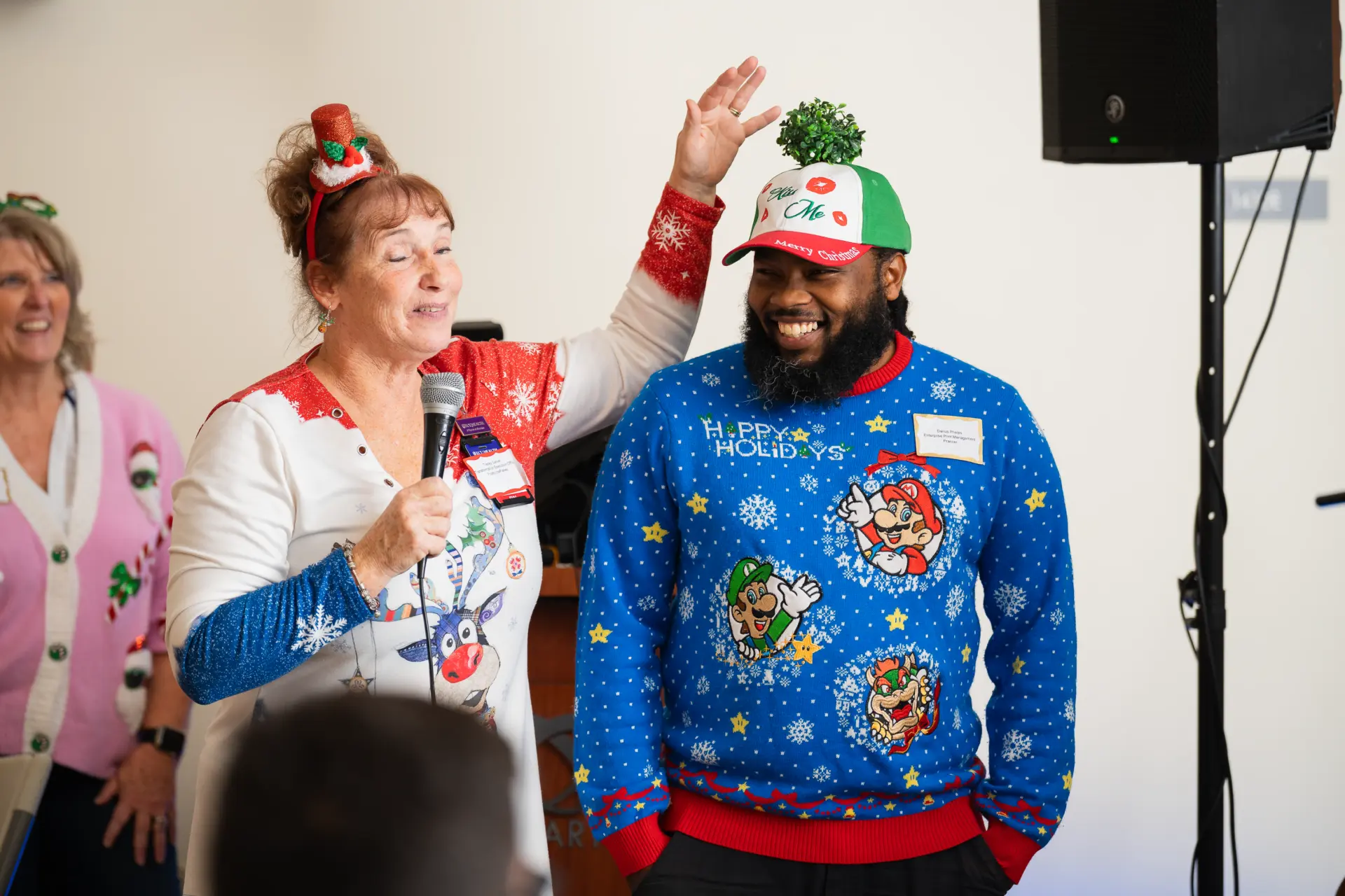 Host in a holiday sweater speaking into a microphone at the party