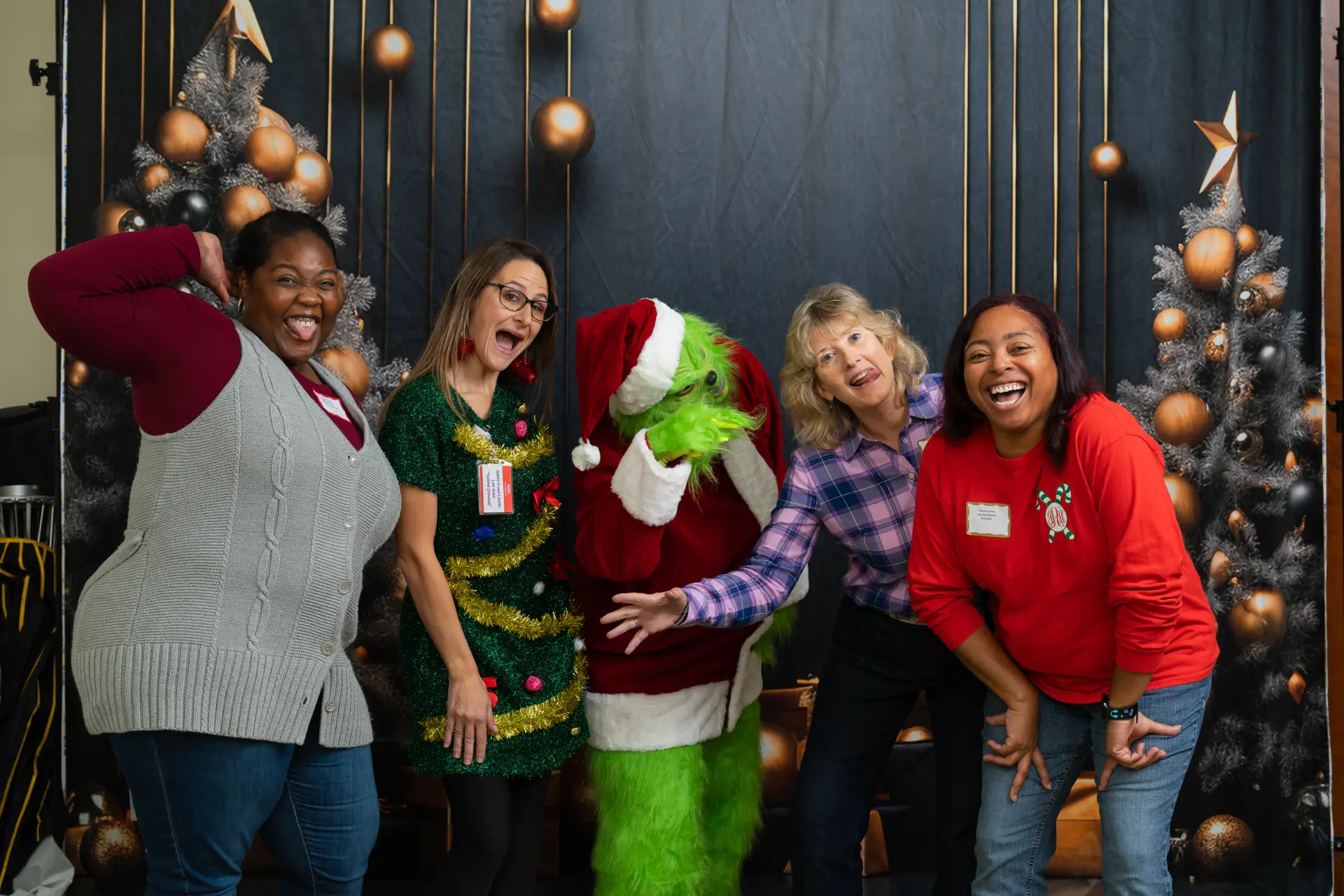 Guests in holiday sweaters laughing with the Grinch character