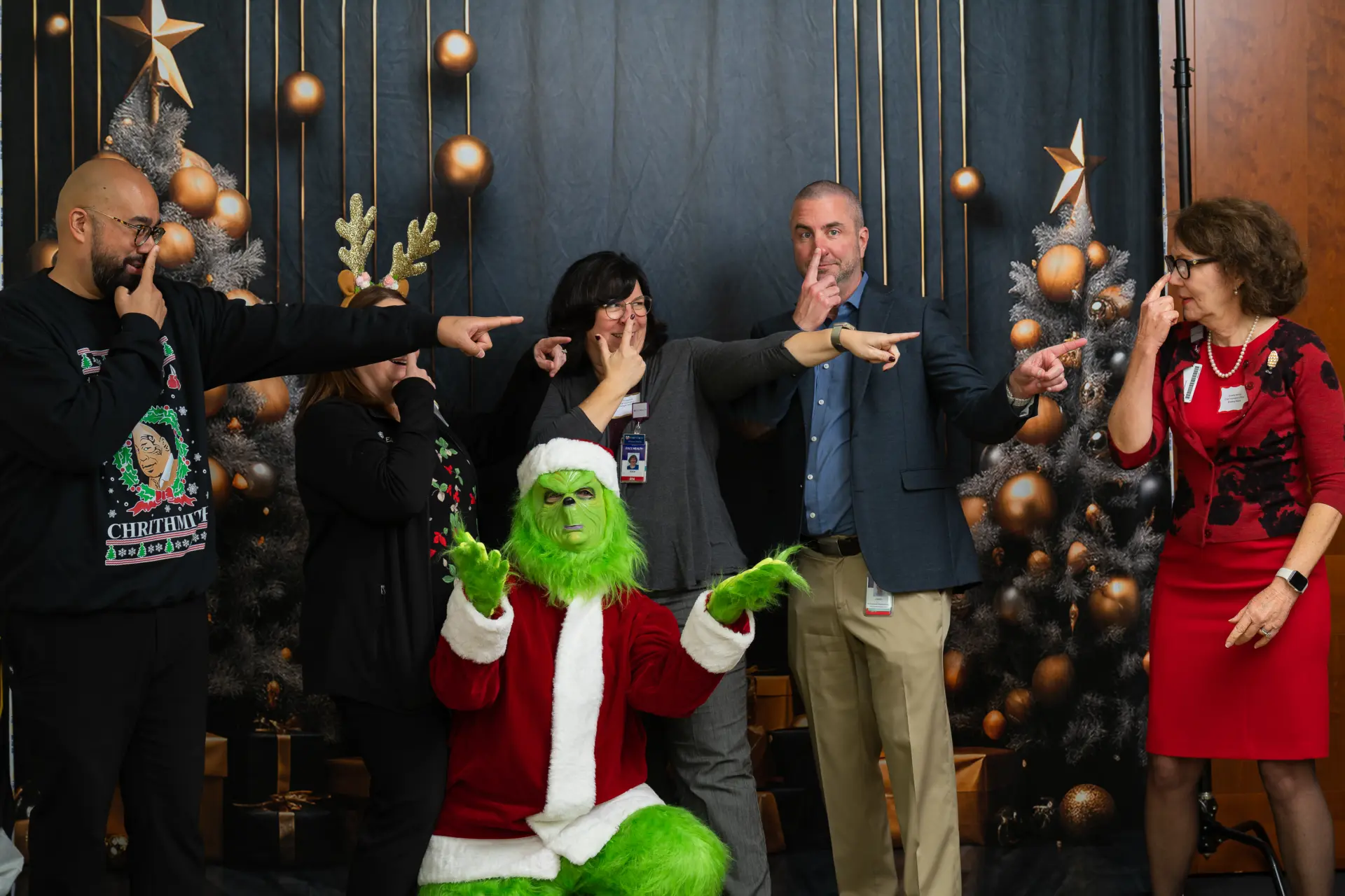 Coworkers celebrating with the Grinch in front of Christmas trees
