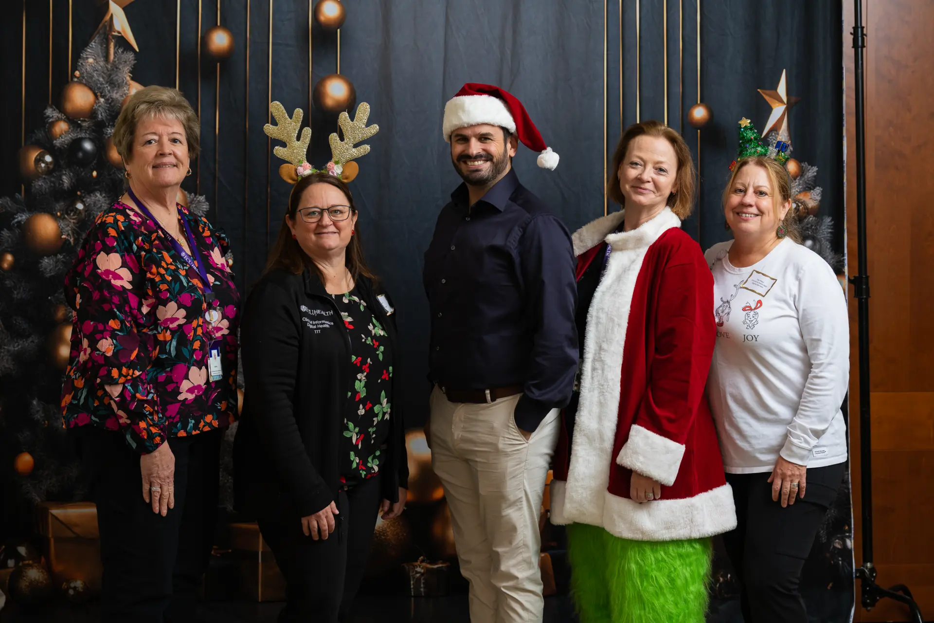 Team members in holiday sweaters lined up in front of decorated trees