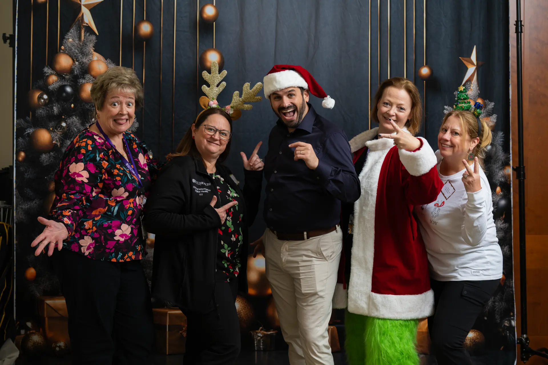 Coworkers in festive hats posing with a Grinch costume character