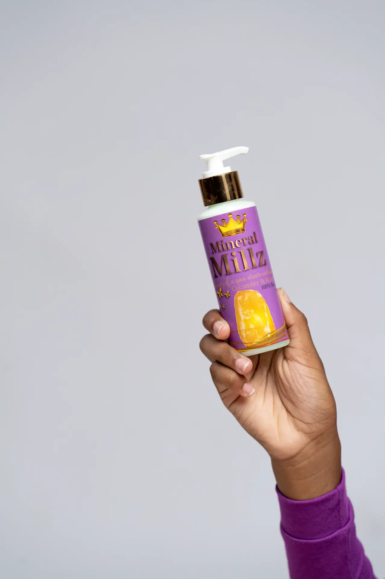 Hand holding up a hair care product bottle against a purple backdrop