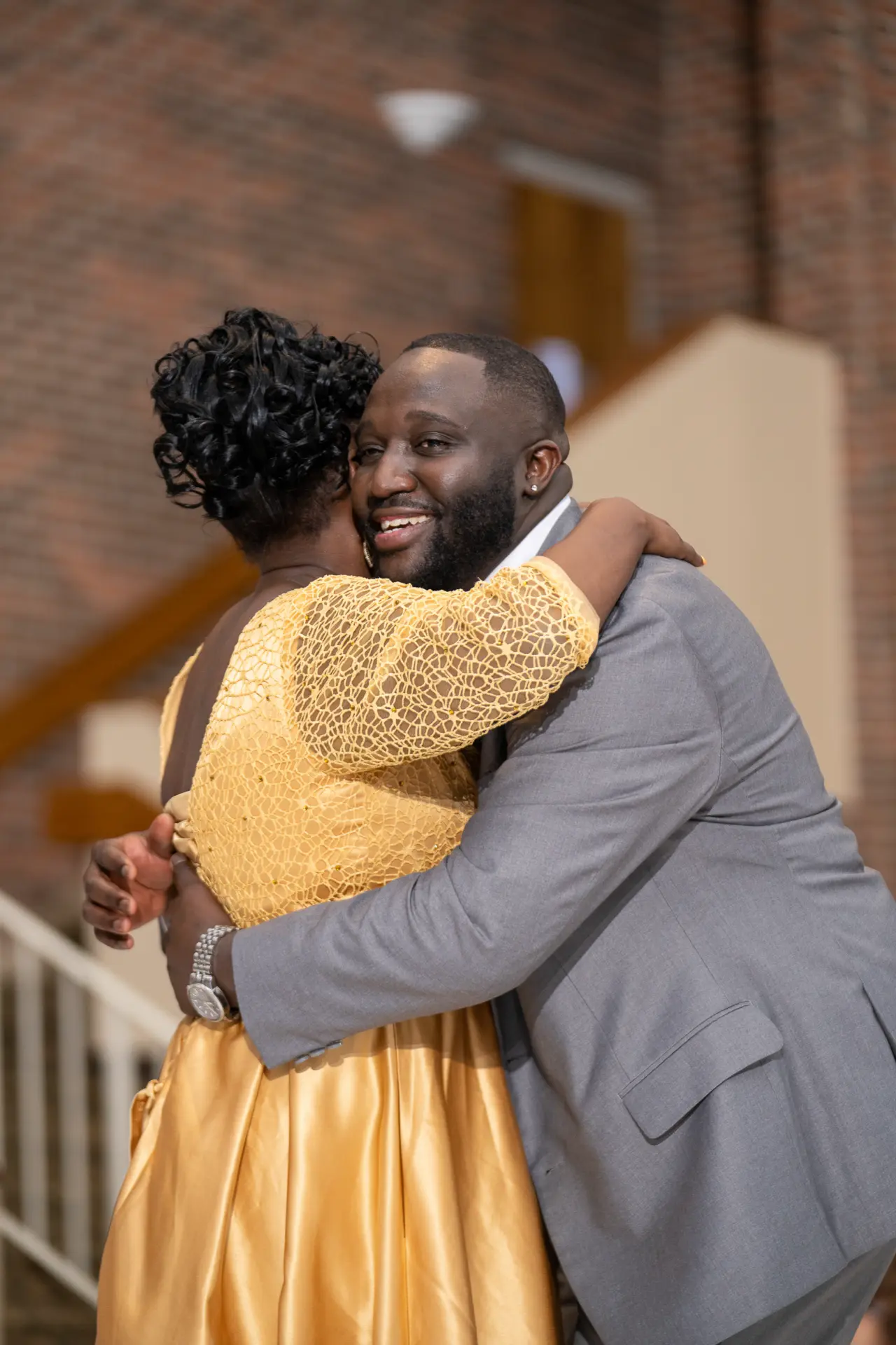 Groom smiling as he embraces a loved one in a golden dress