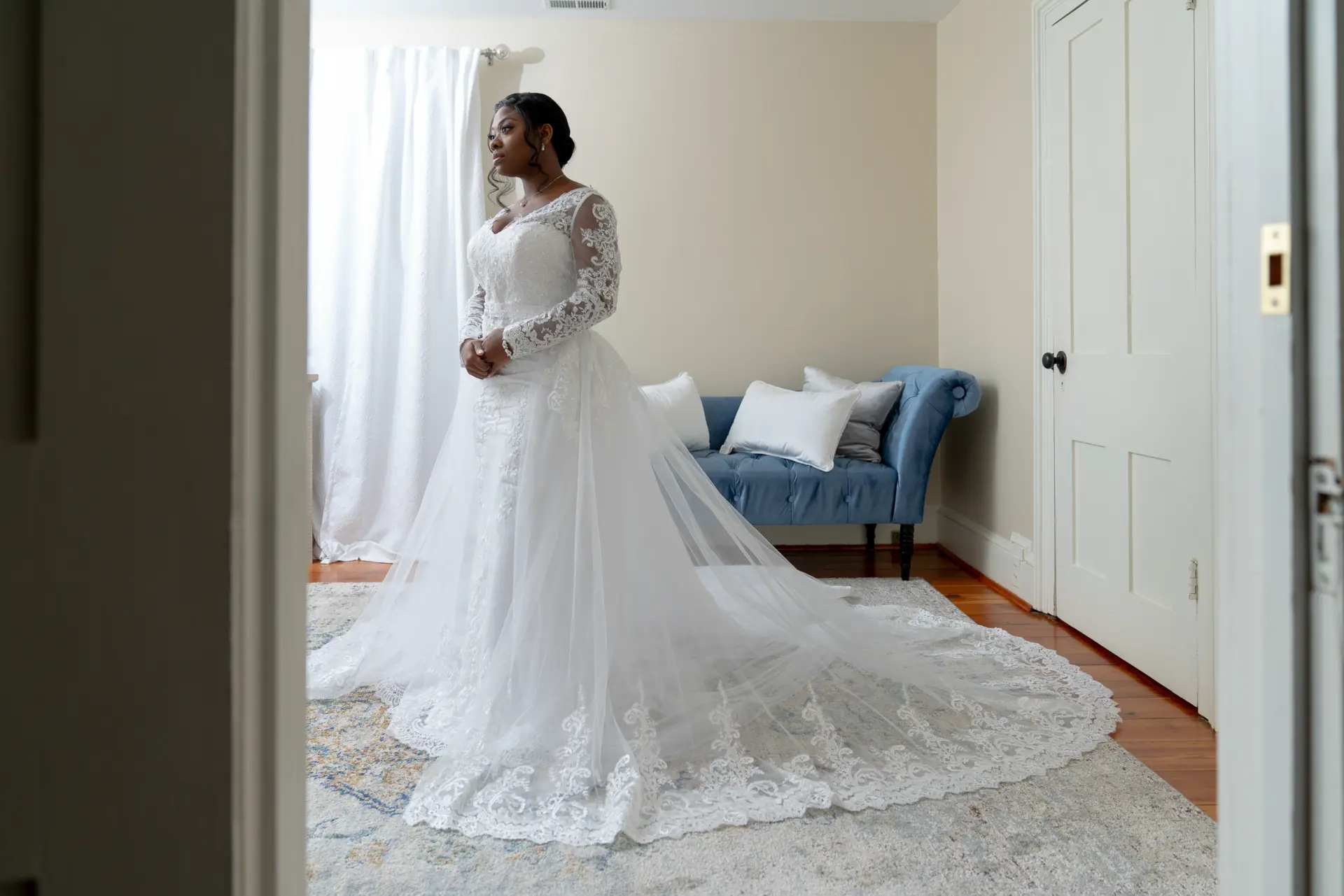 Bride in her ball gown standing in a sunlit bedroom doorway before the ceremony