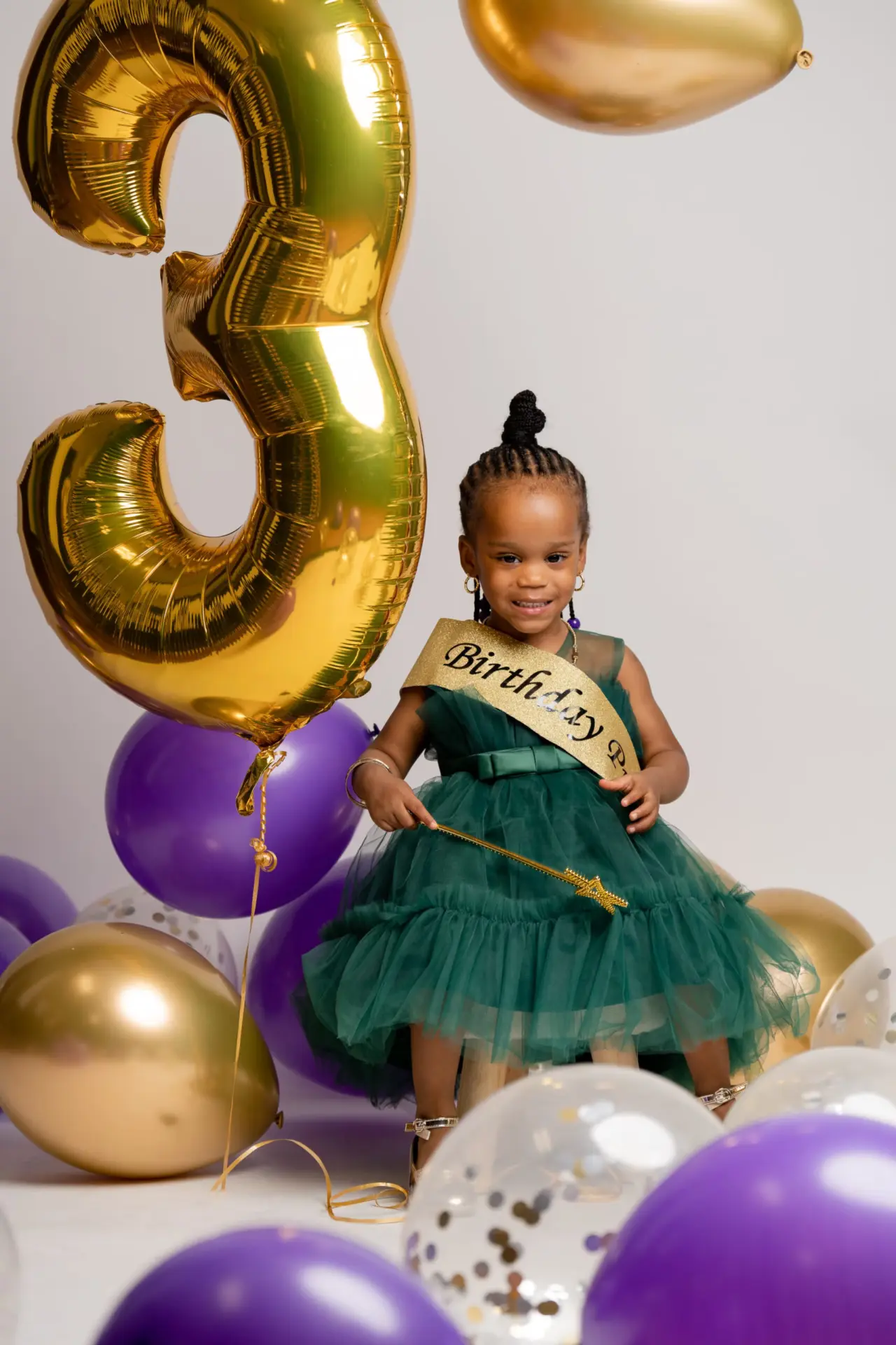 Little girl in a green dress beside a gold "3" balloon for her birthday