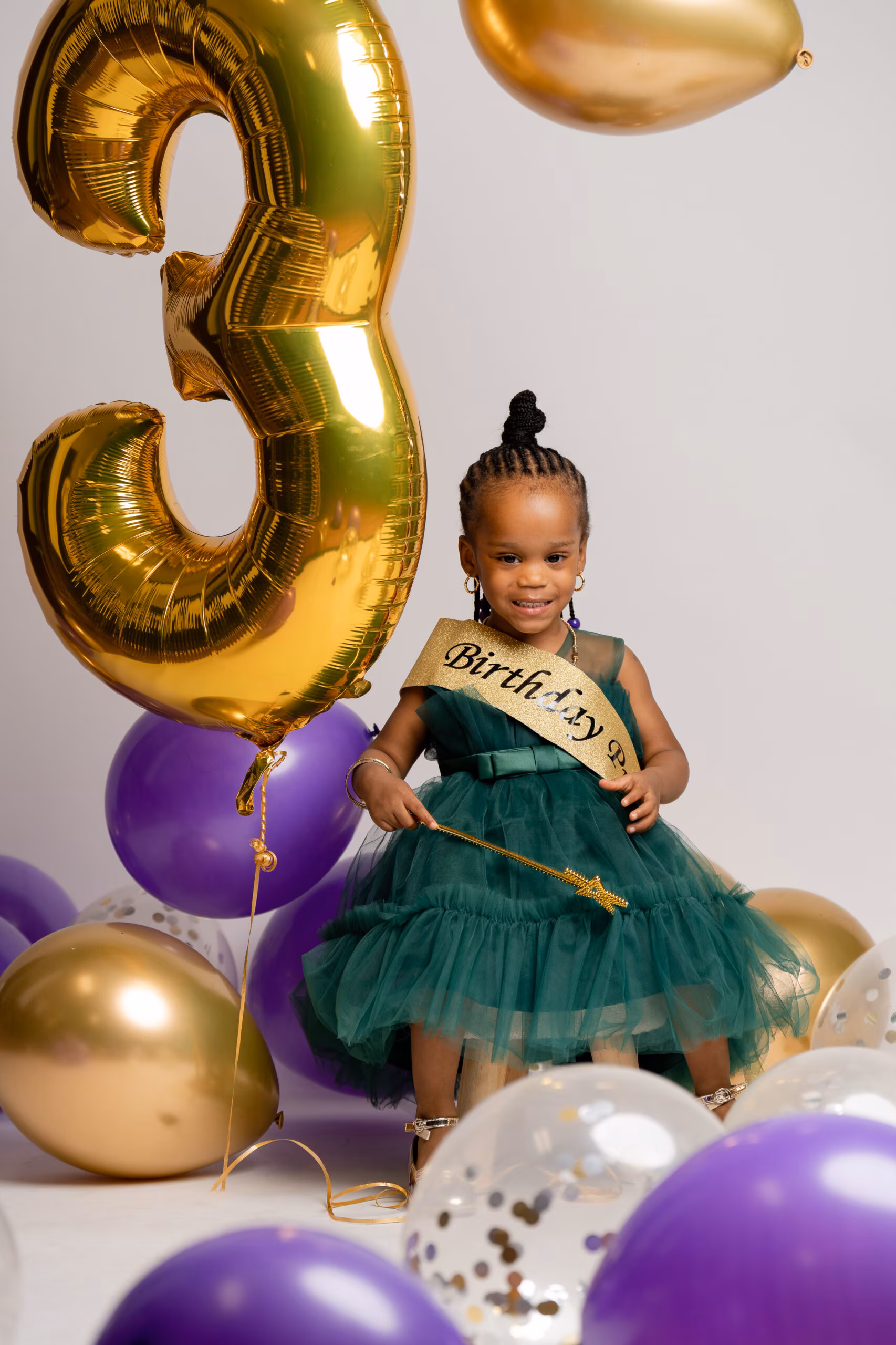 Little girl in a green dress beside a gold "3" balloon for her birthday