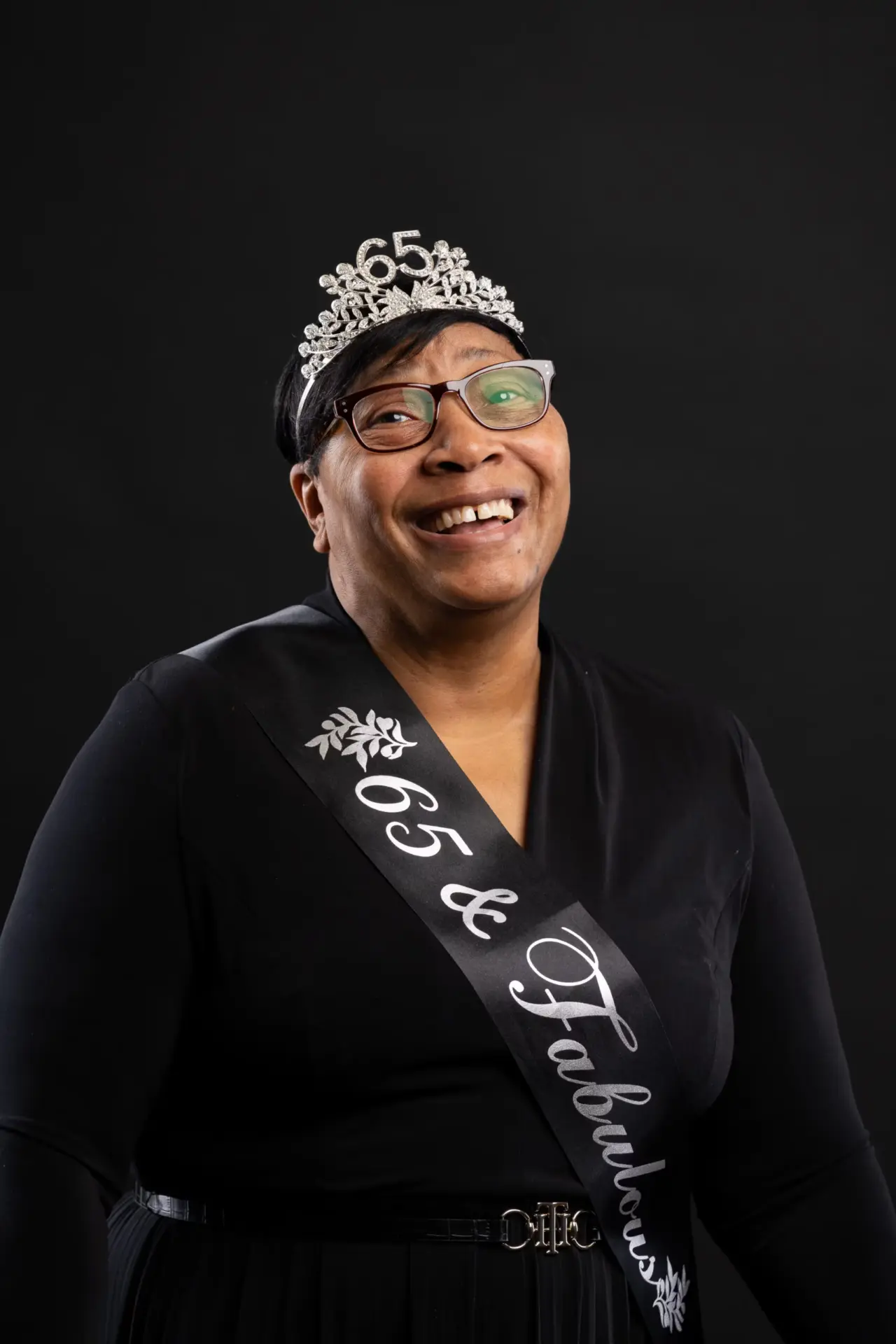 Smiling woman in a tiara and birthday sash against black
