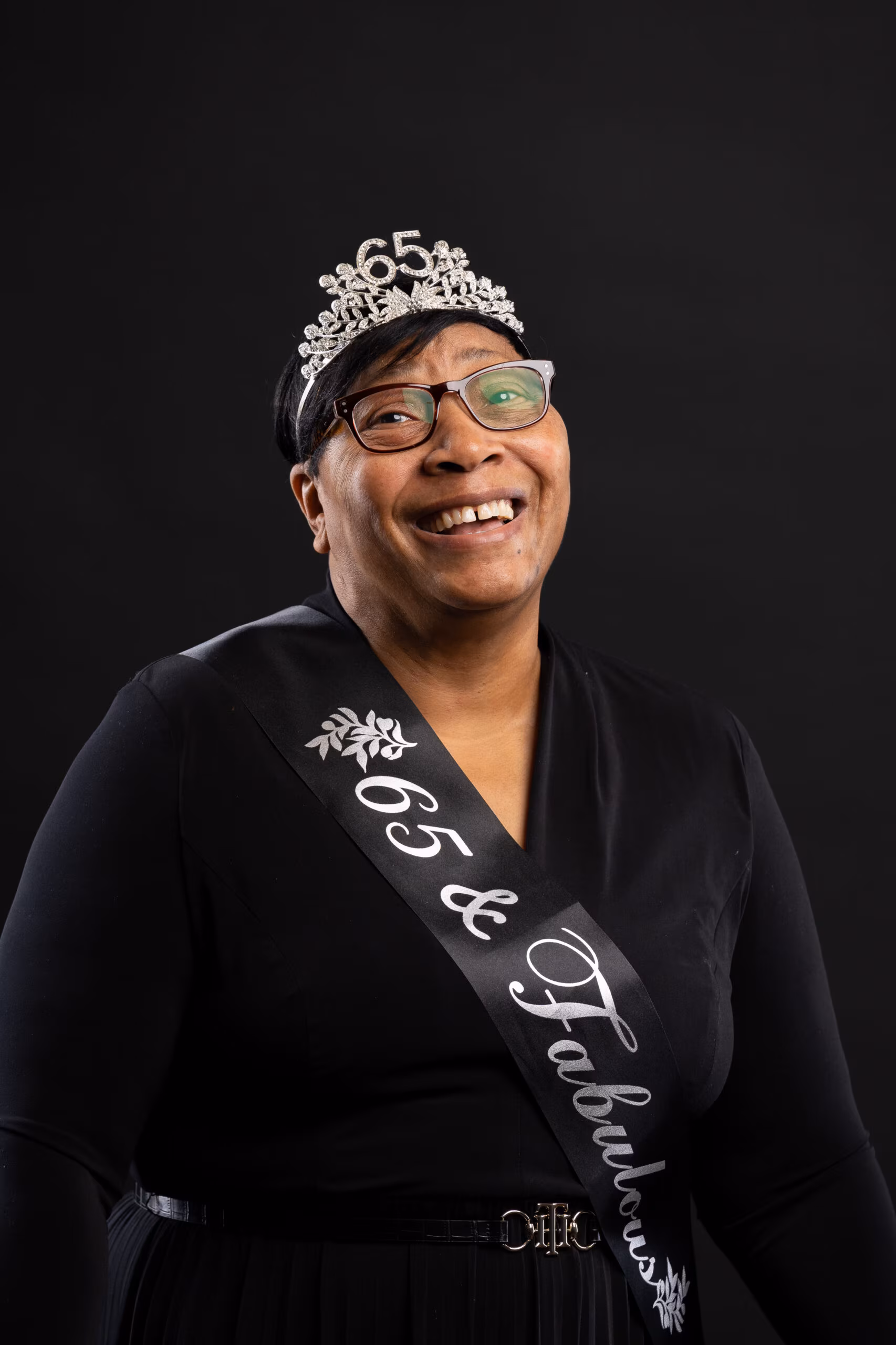 Smiling woman in a tiara and birthday sash against black