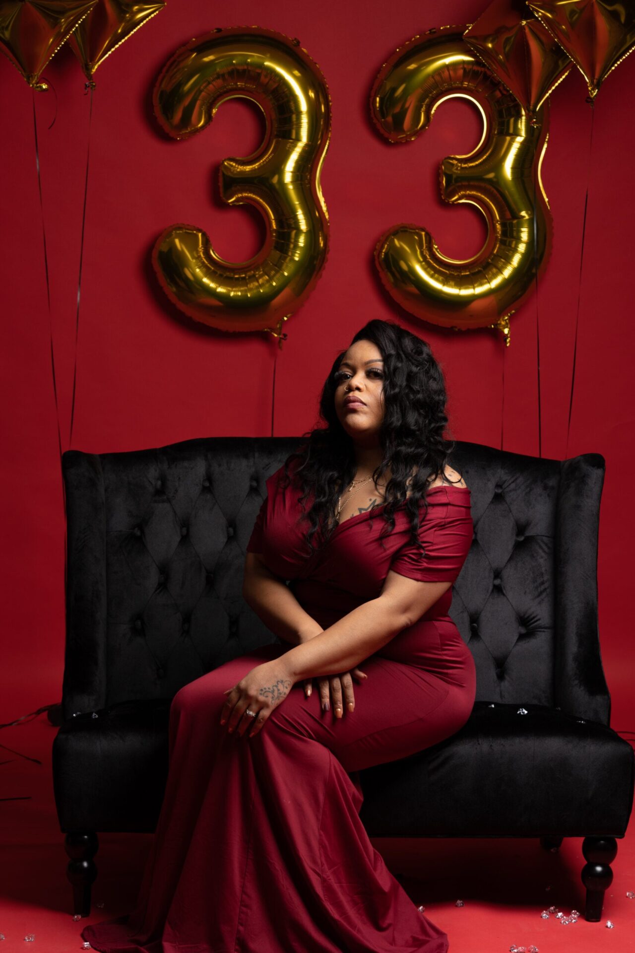 Woman in burgundy on a velvet couch with gold "33" balloons