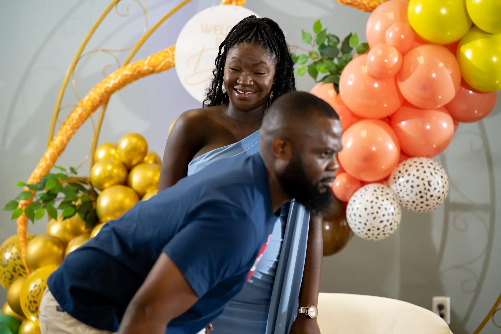 Man kneeling in front of a woman beside a peach balloon arch