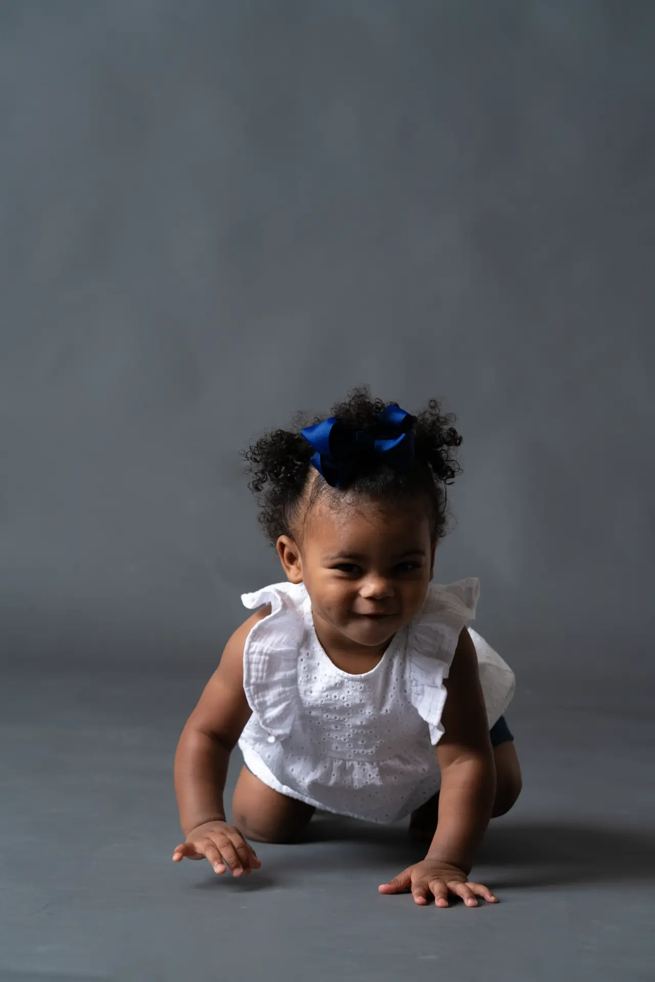 Baby in white crawling on a gray studio backdrop