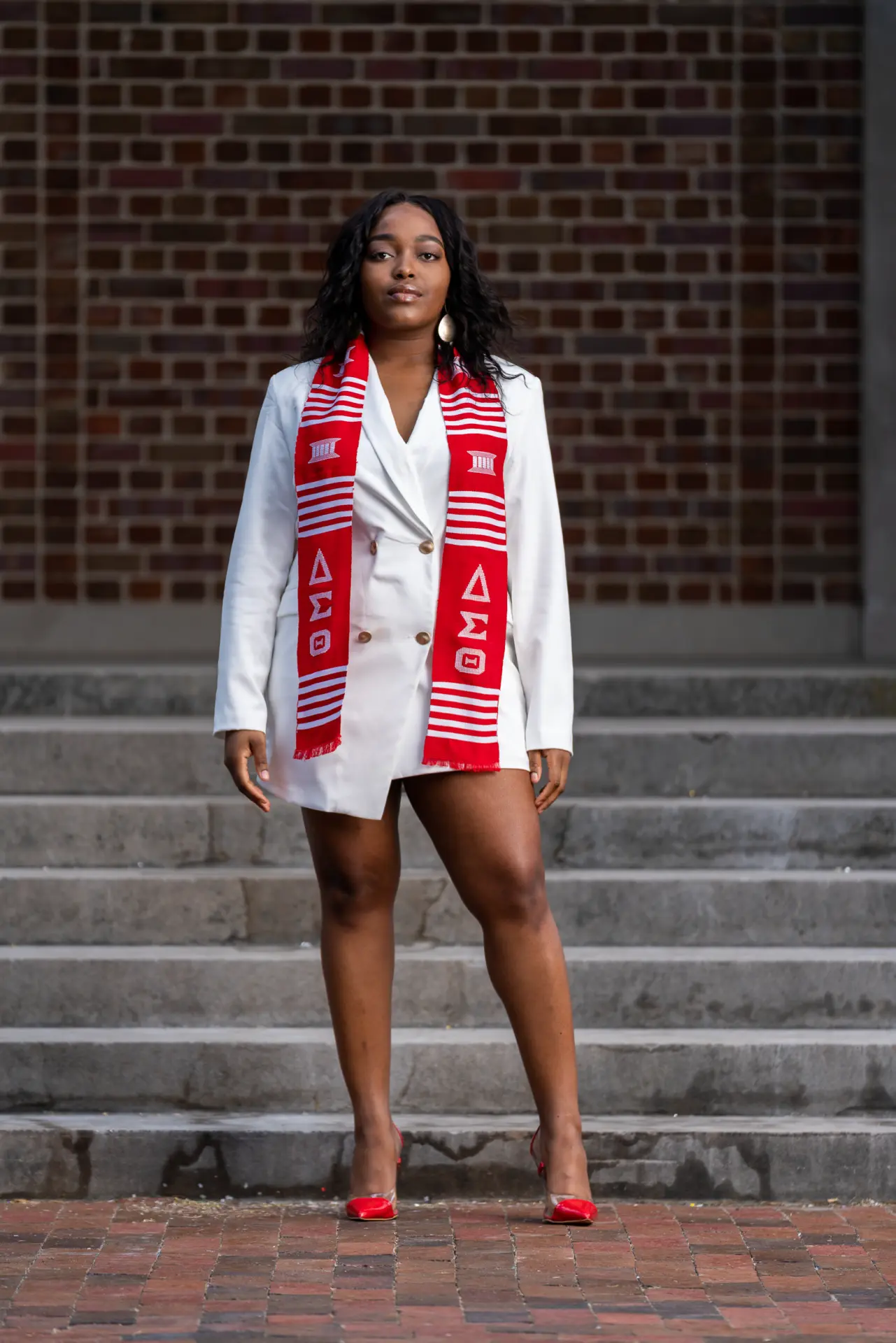 Graduate in a white jacket and red stole standing on brick steps