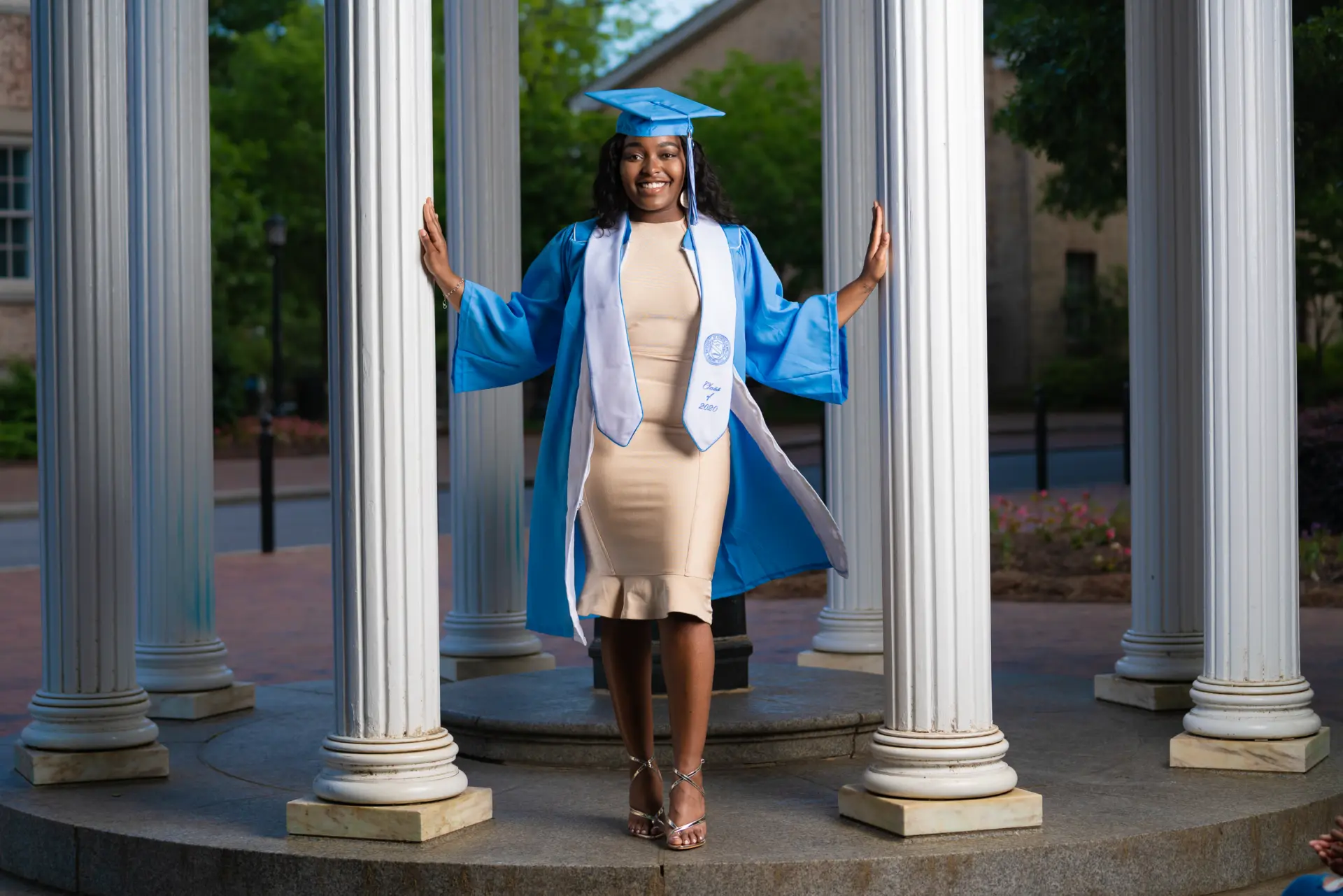 Graduate in a blue gown and cap posing in a columned pavilion