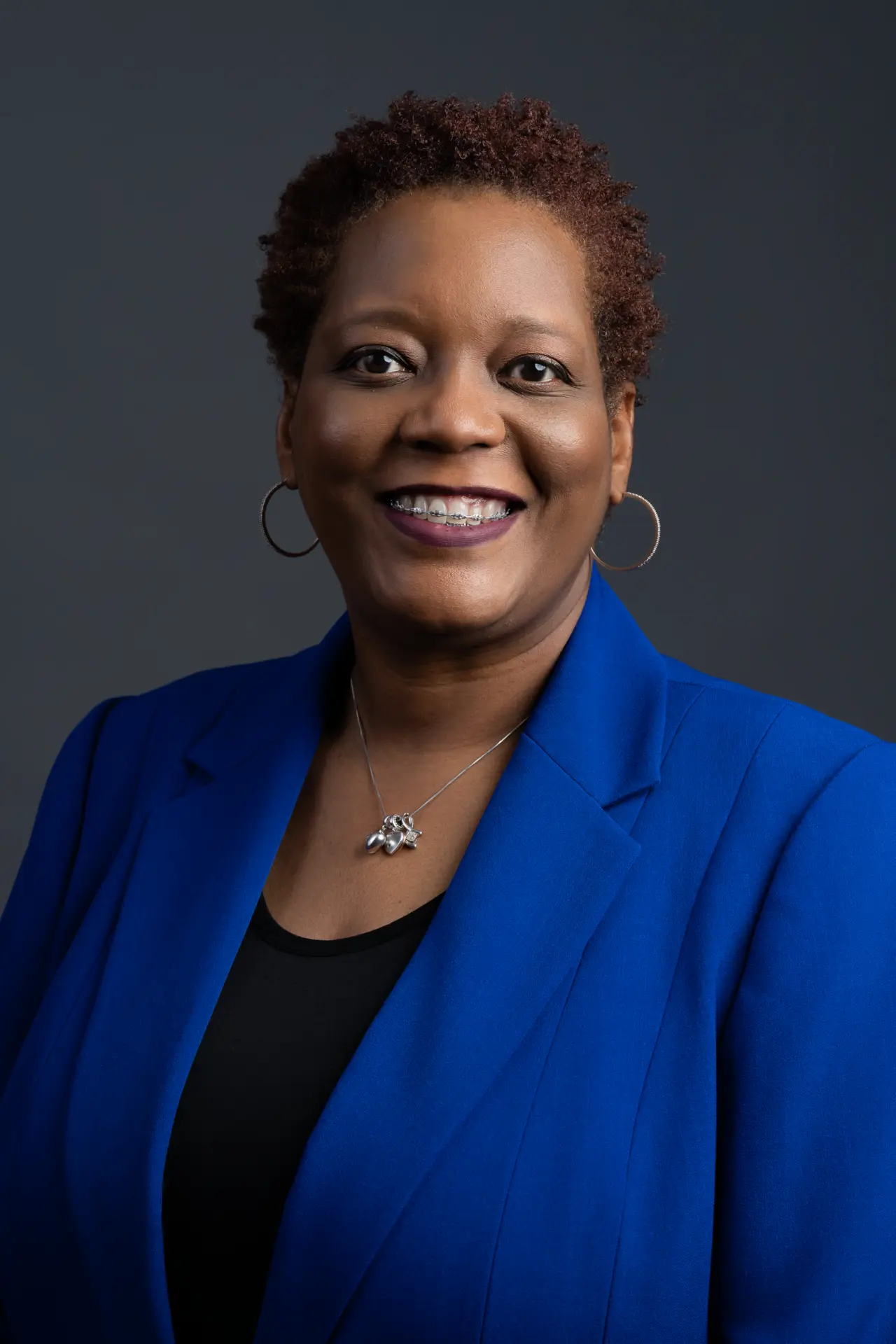 Woman in a royal blue blazer, professional headshot on dark gray