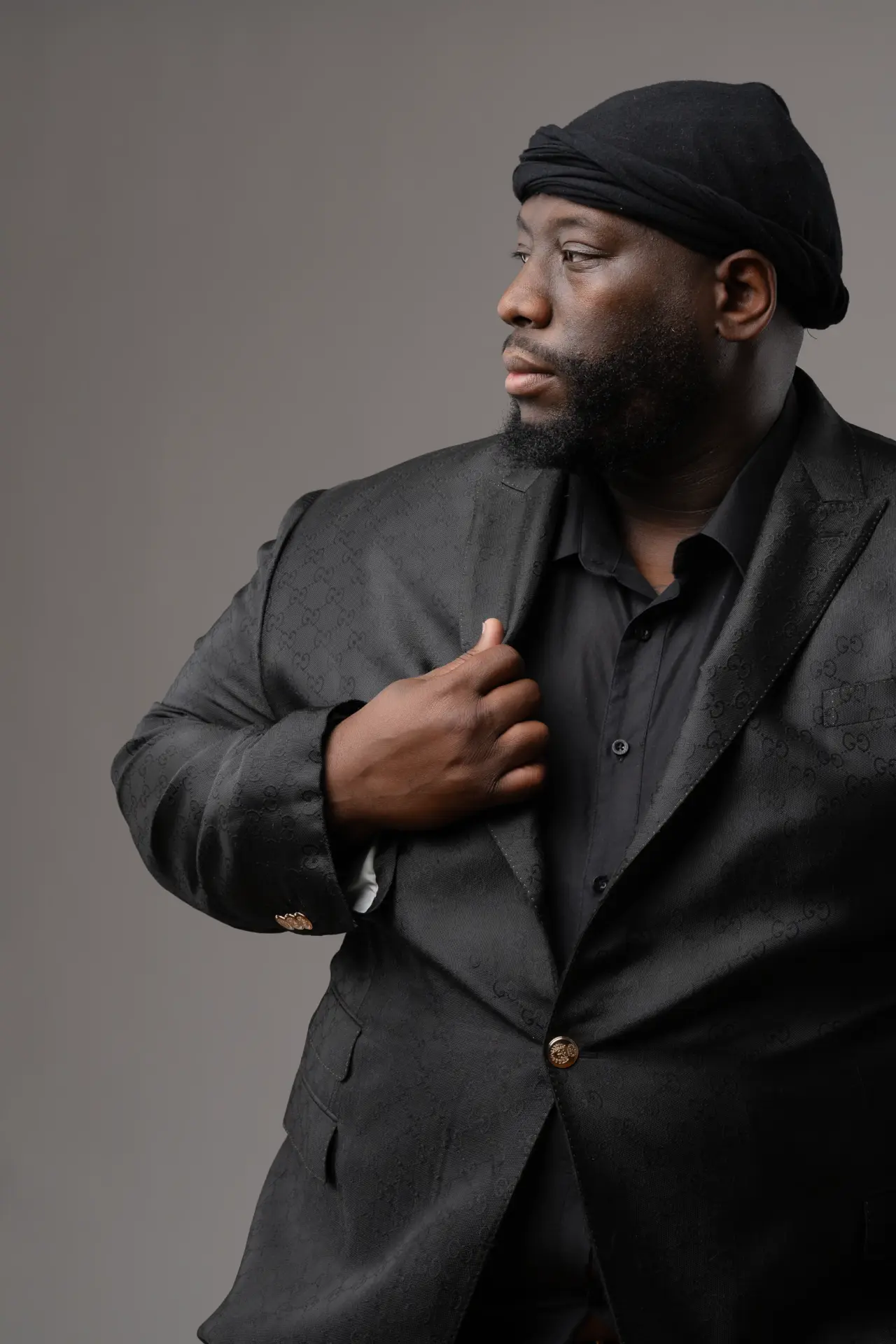 Man in a cap and dark jacket posing confidently on gray