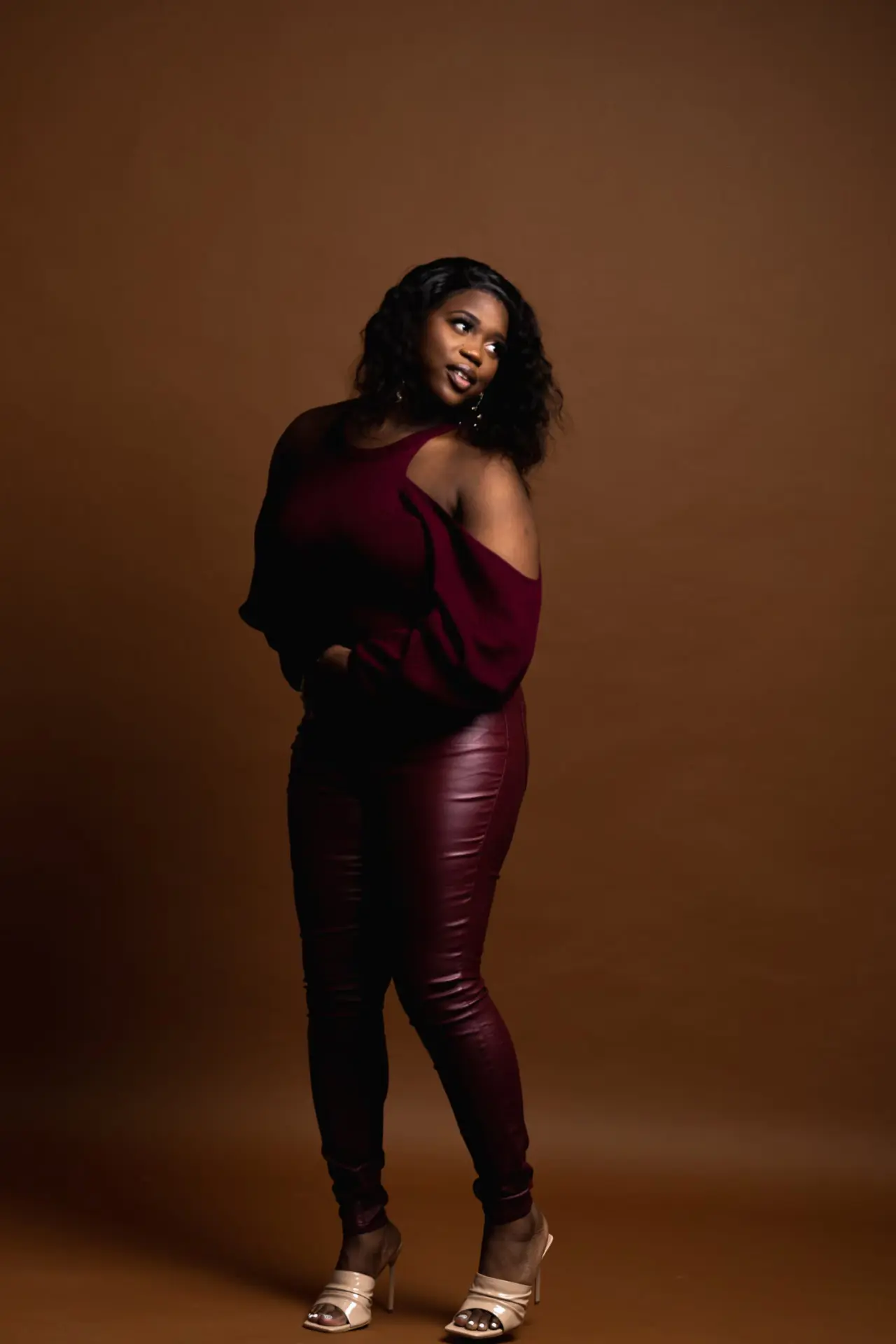 Woman in a burgundy top posing against brown