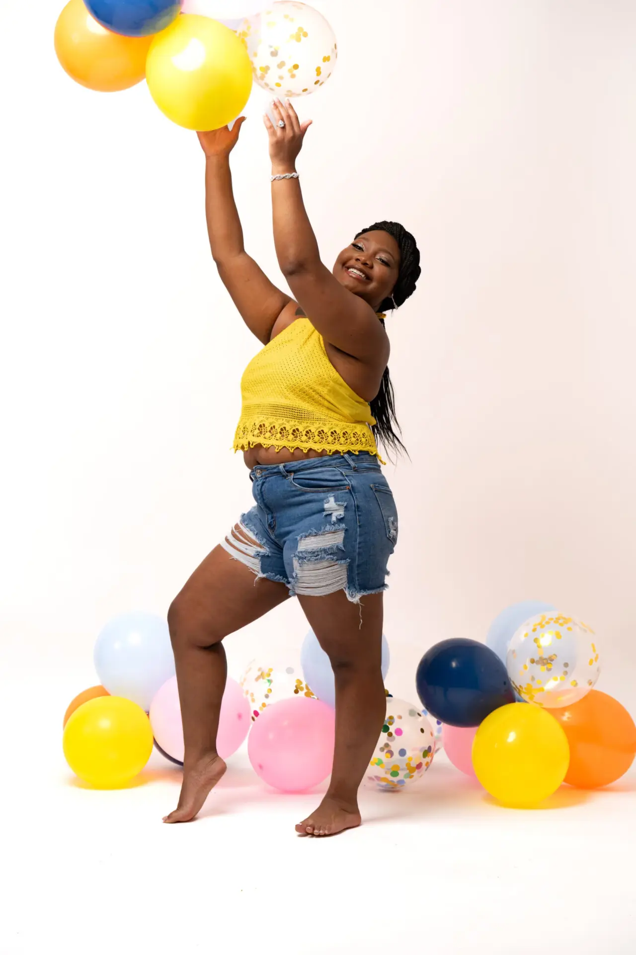 Woman in yellow catching balloons on a white backdrop