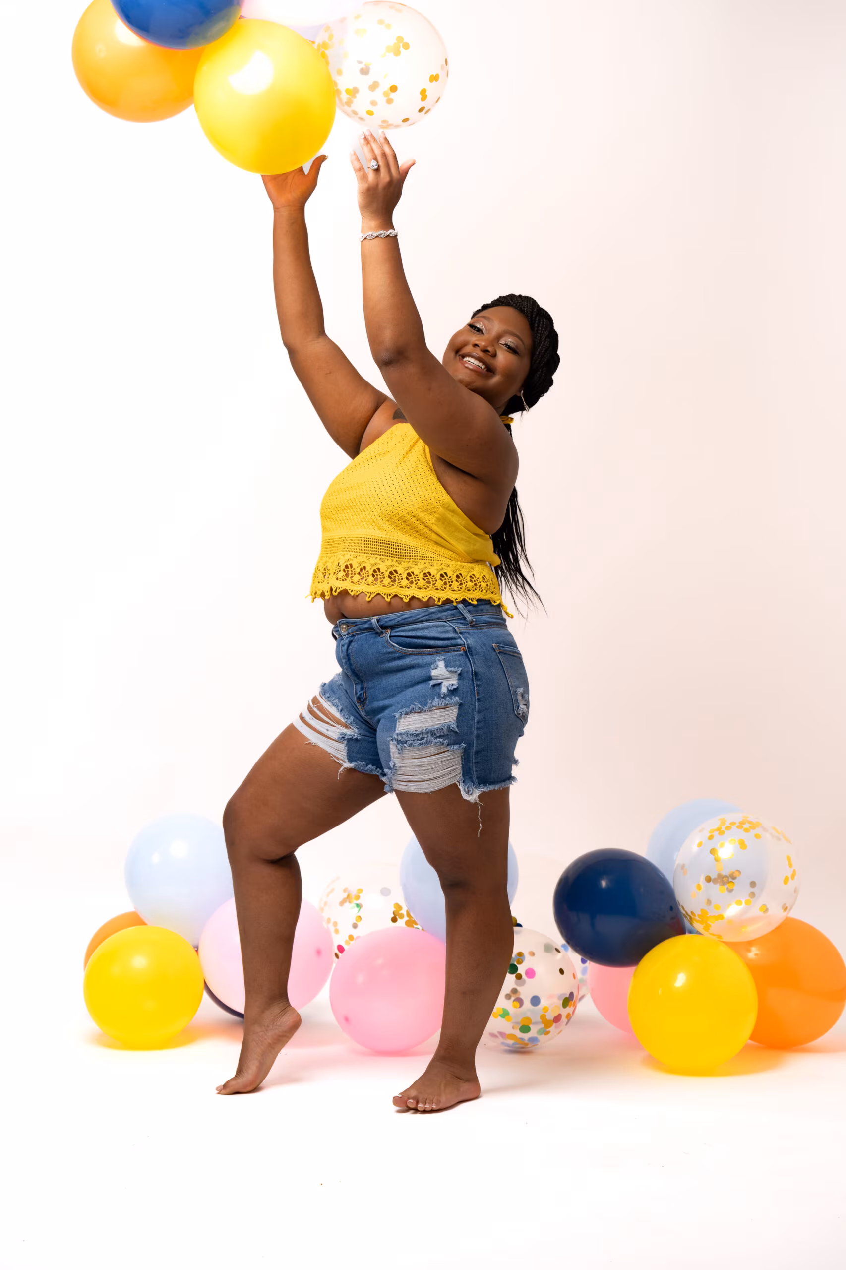 Woman in yellow catching balloons on a white backdrop