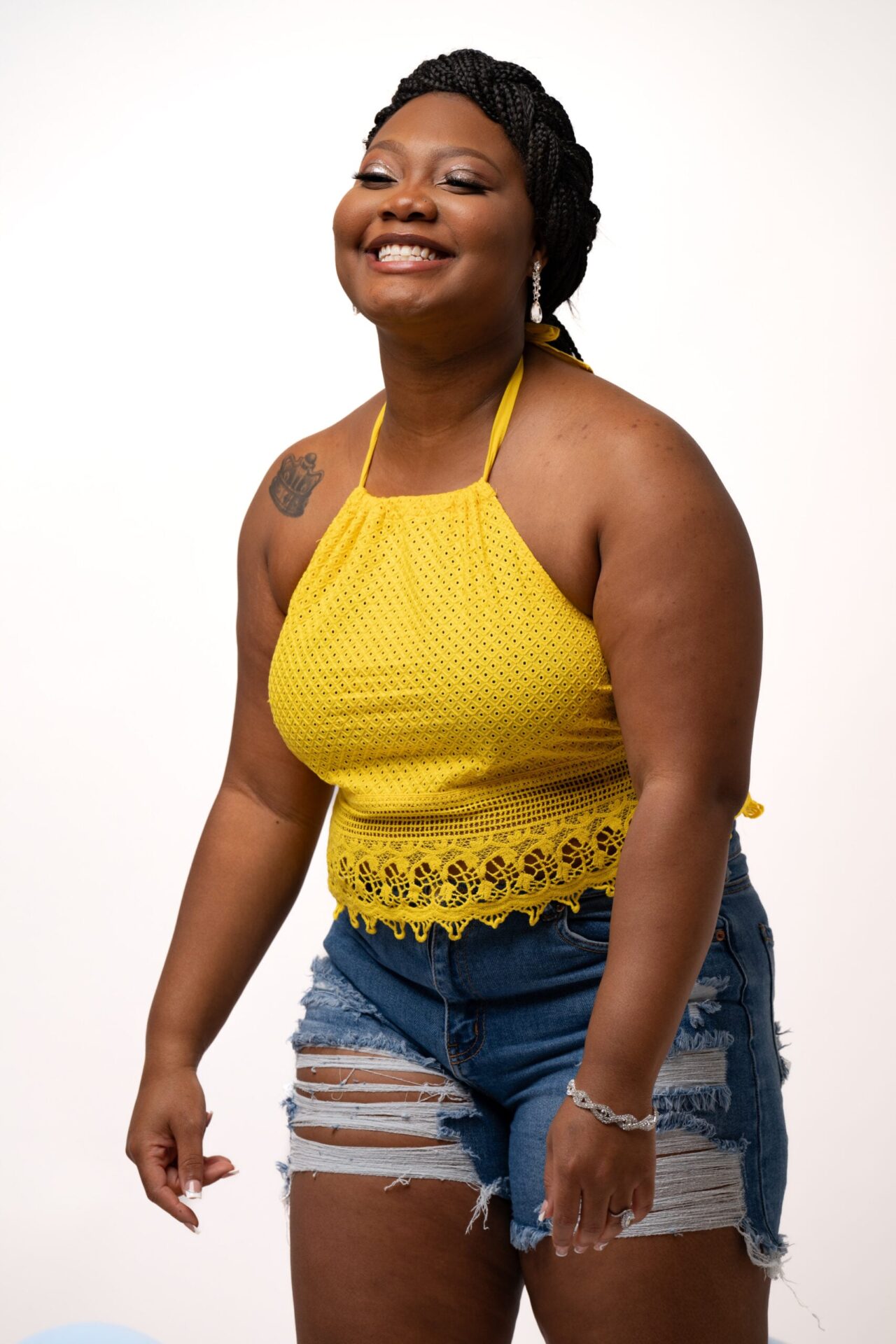 Smiling woman in a yellow halter and denim shorts on white