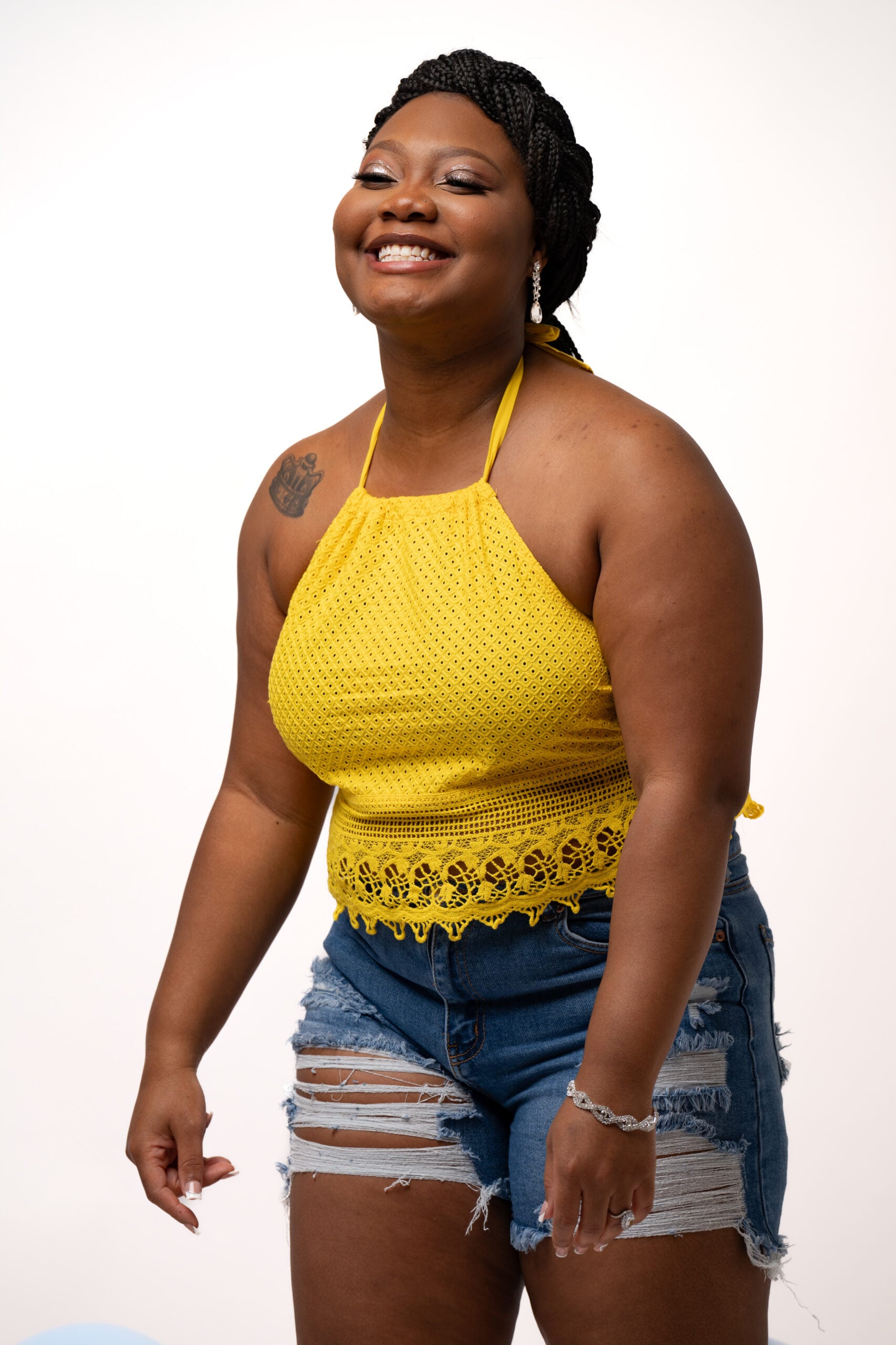Smiling woman in a yellow halter and denim shorts on white