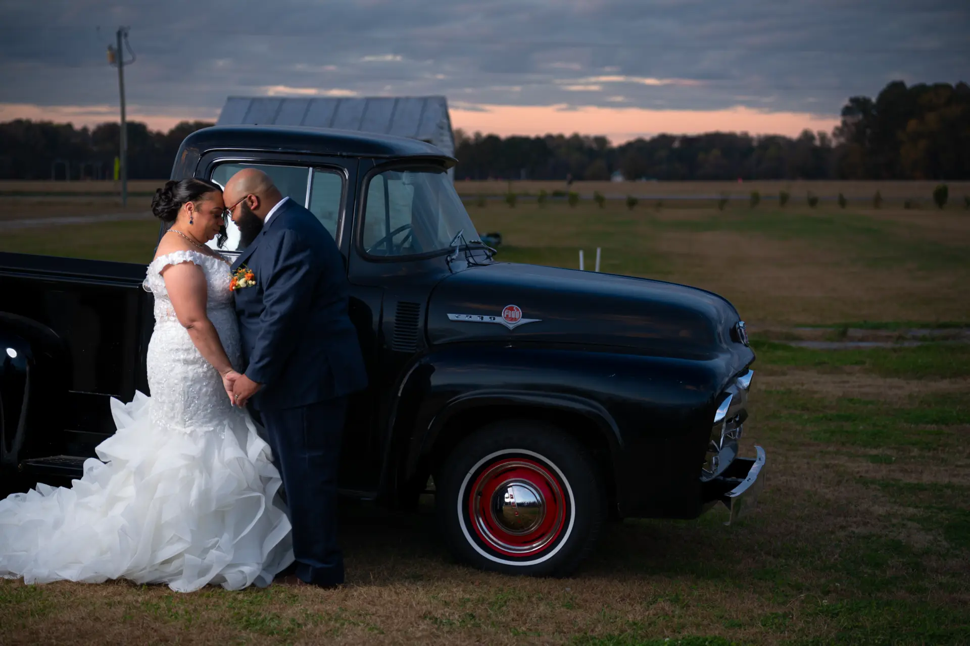 Couple poses with a vintage black pickup truck in a field