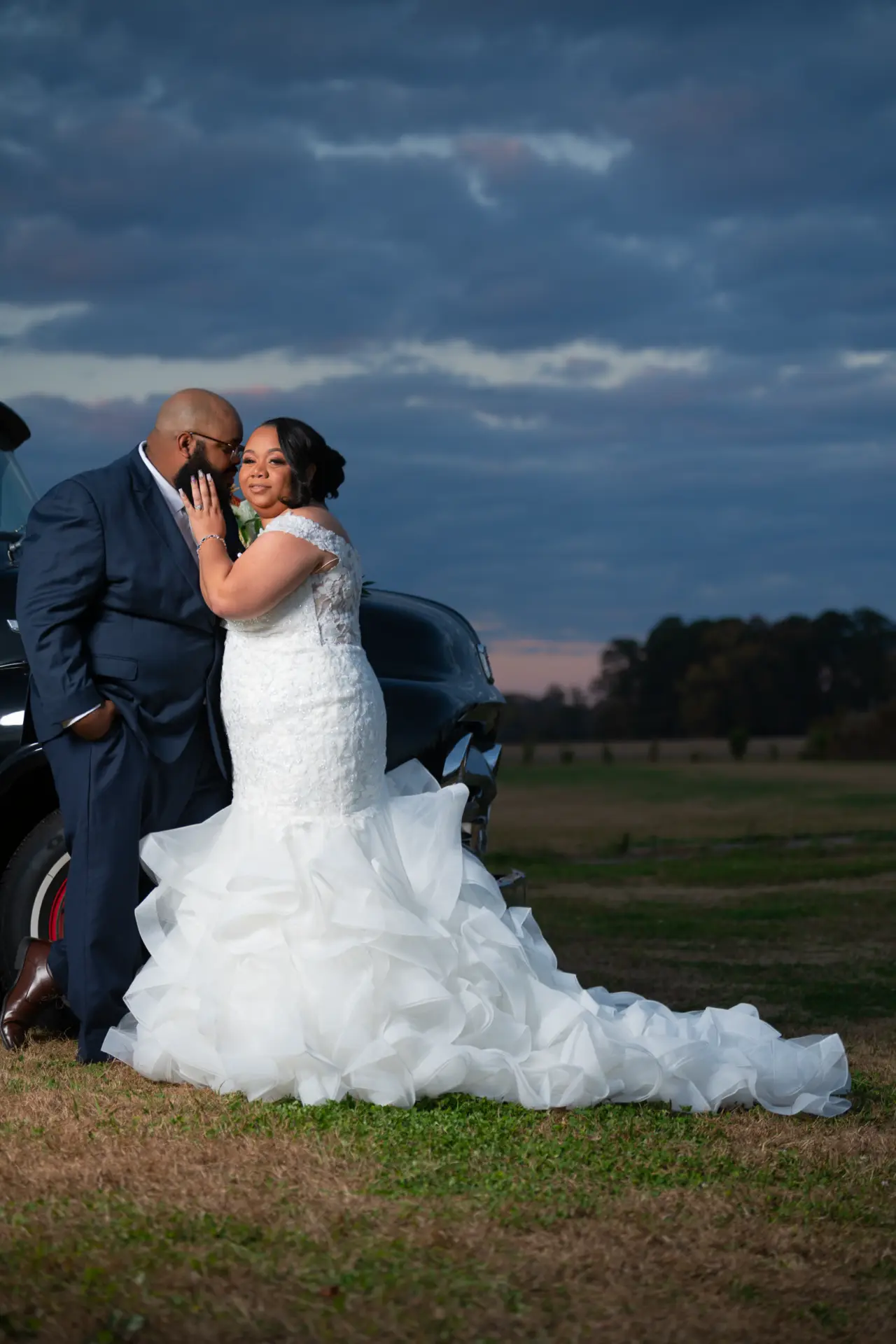 Bride and groom kiss in a field under a dramatic evening sky