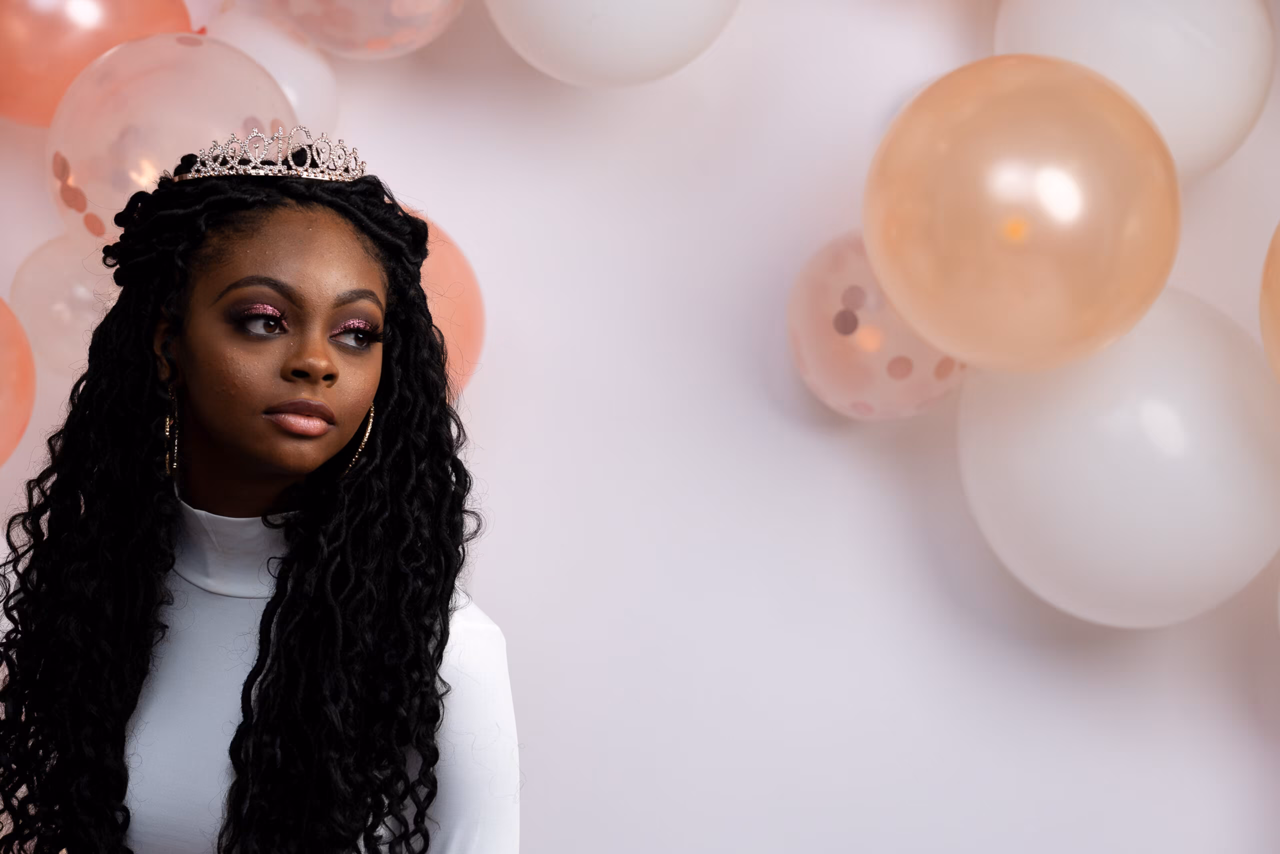 Woman in a tiara beside peach and white balloons