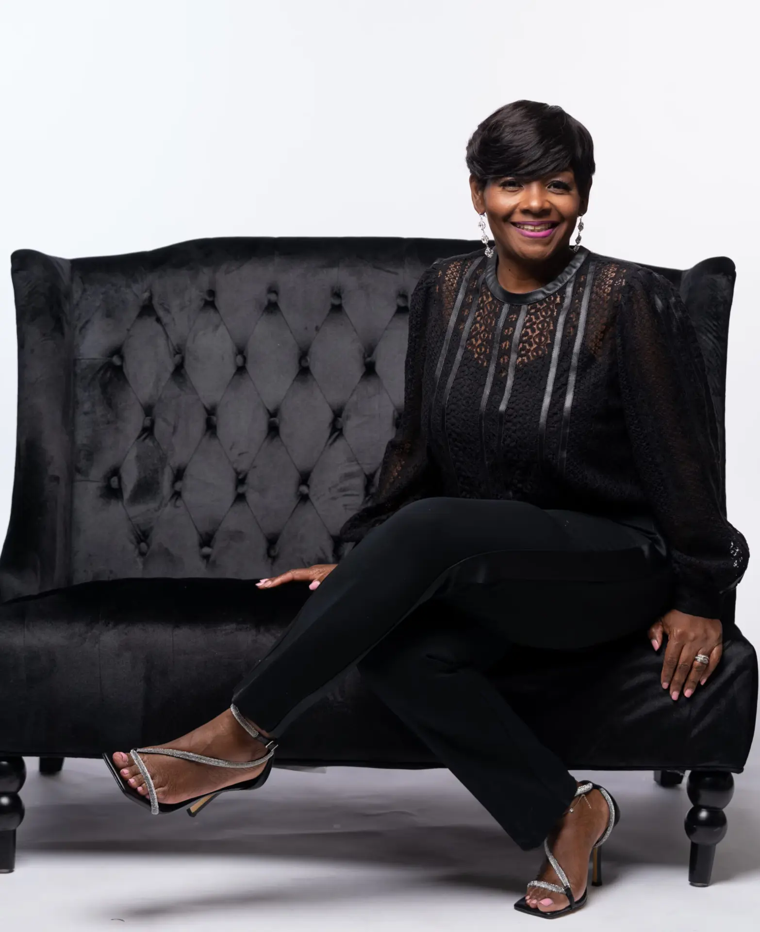 Woman in black lounging on a tufted black sofa