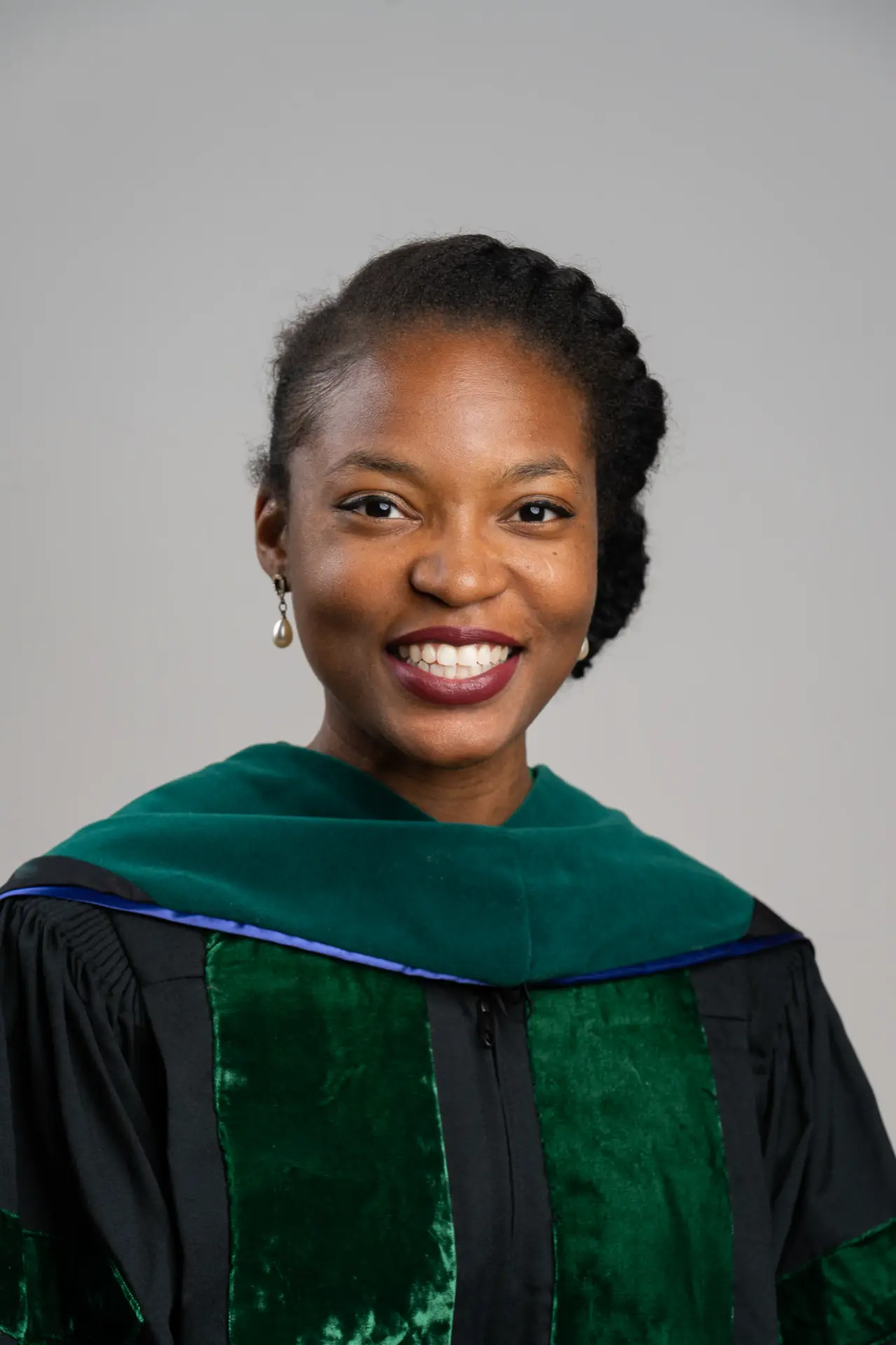 Smiling woman in green and black doctoral robes, studio portrait