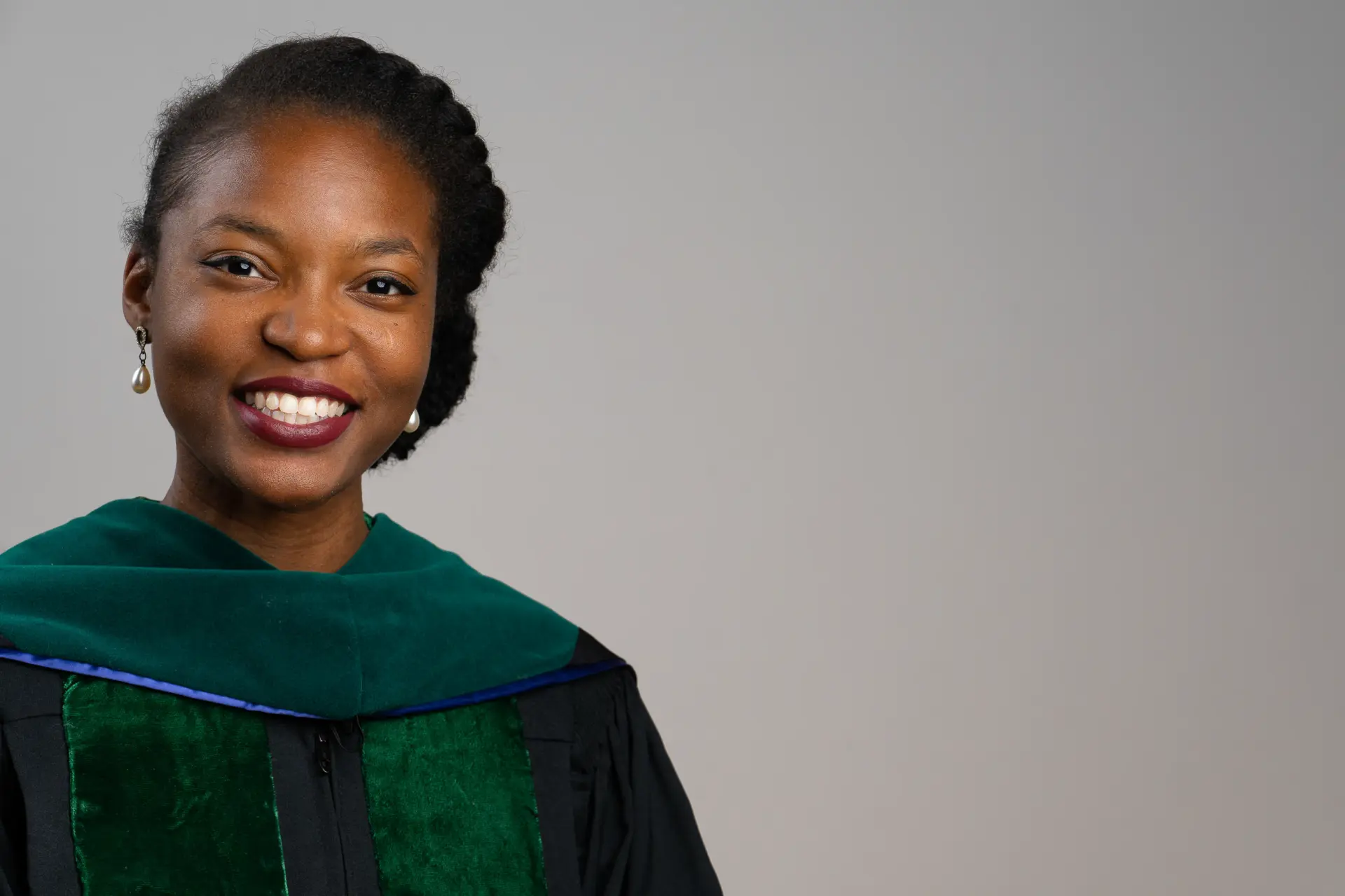 Woman in green doctoral regalia, headshot on gray